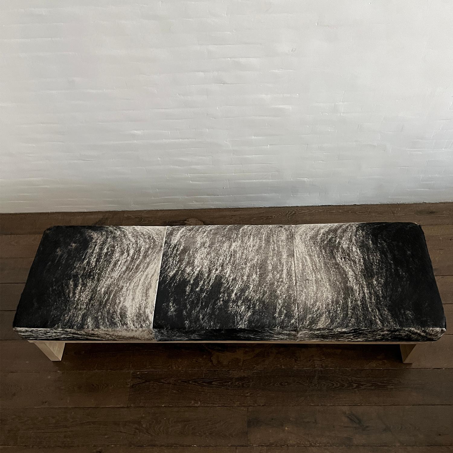 Soft, minimalist forms combine into a bench / ottoman with a sculptural base that celebrates wood and the legacy of French designer Pierre Jeanneret. Solid Washed Oak base. Seat upholstered with a gorgeous natural Hair on hide, in a mottled brindle