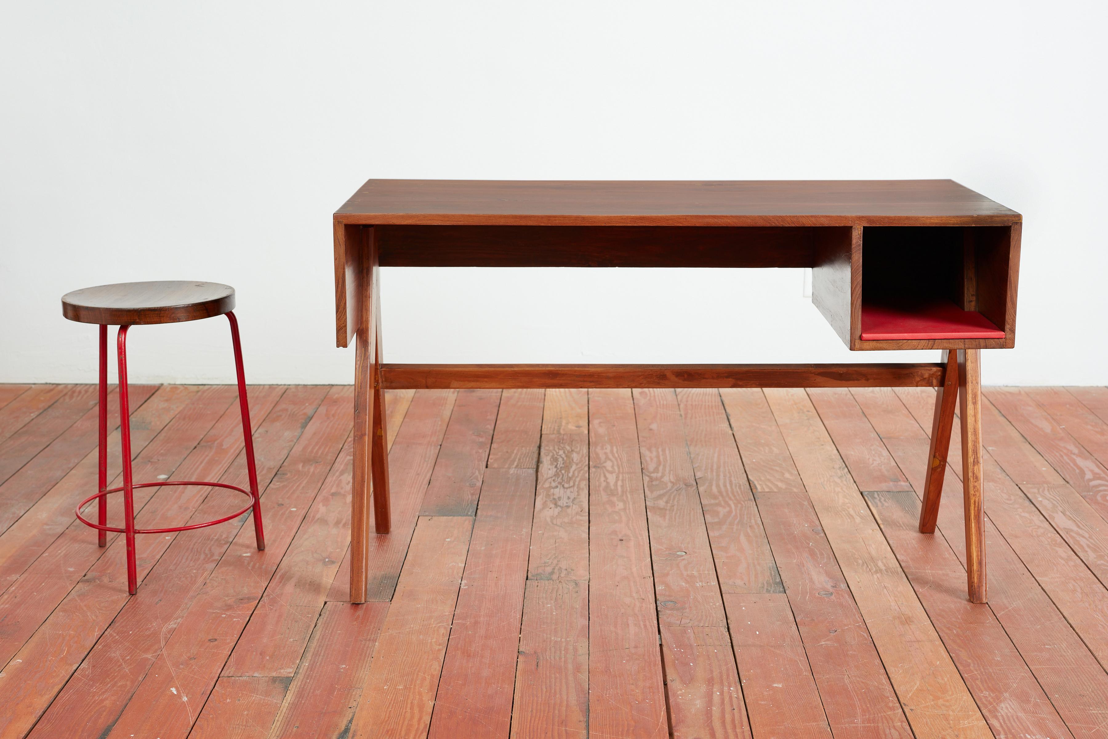 Pierre Jeanneret desk and stool from Chandigarh
France/India, c. 1960
Constructed of teak wood, stool has red enameled steel, and red vinyl inside storage cubby. 

desk: 29¼ h × 47¾ w × 23¾ d in (74 × 121 × 60 cm)
stool: 21½ h × 14¾ dia in (55 × 37