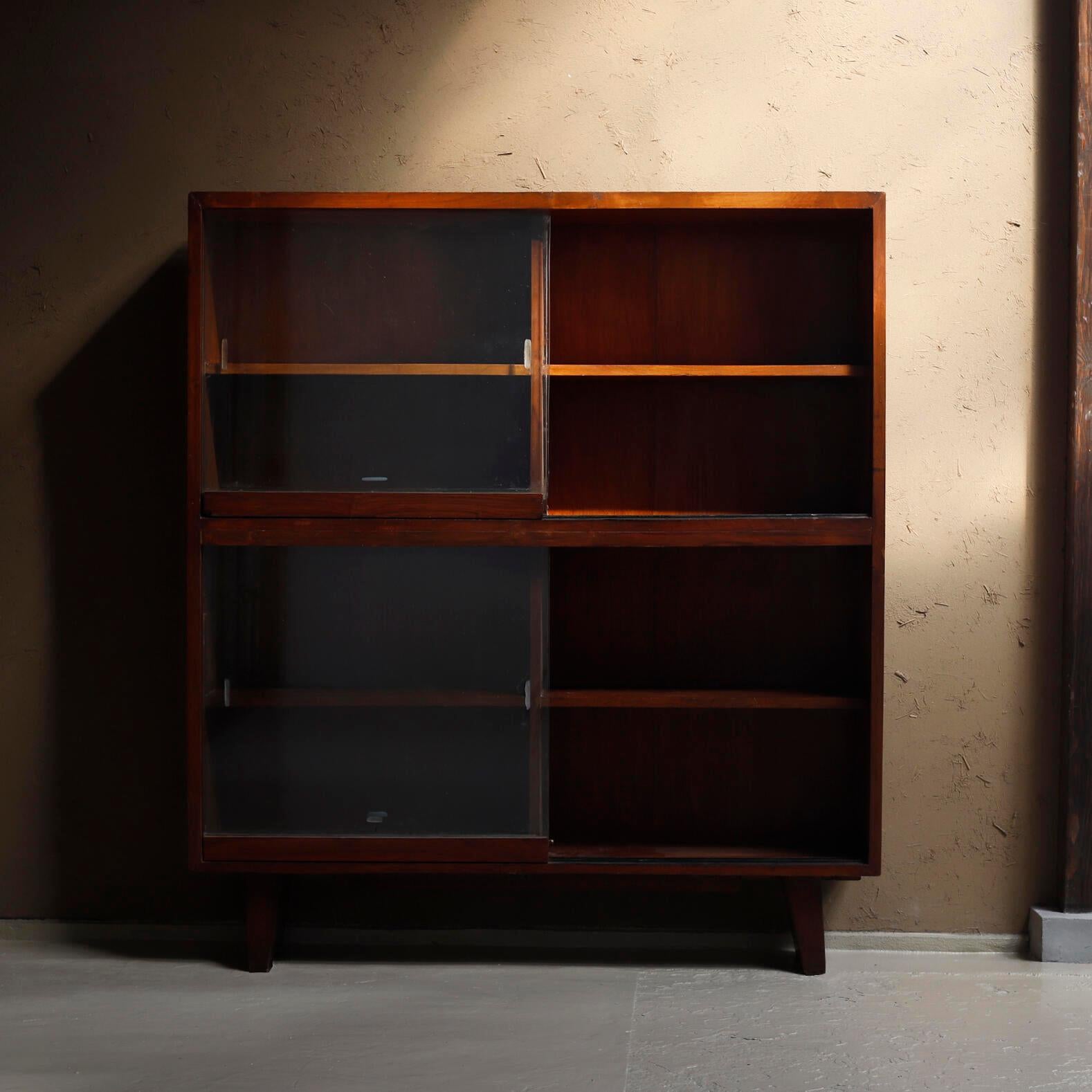 Teak glass fronted bookcase designed by Pierre Jeanneret for Chandigarh.
Thick teak solid wood shelves inside.
The glass sliding doors on the bottom are alterations to the original ones.

Provenance: Administrative buildings, Chandigarh, India