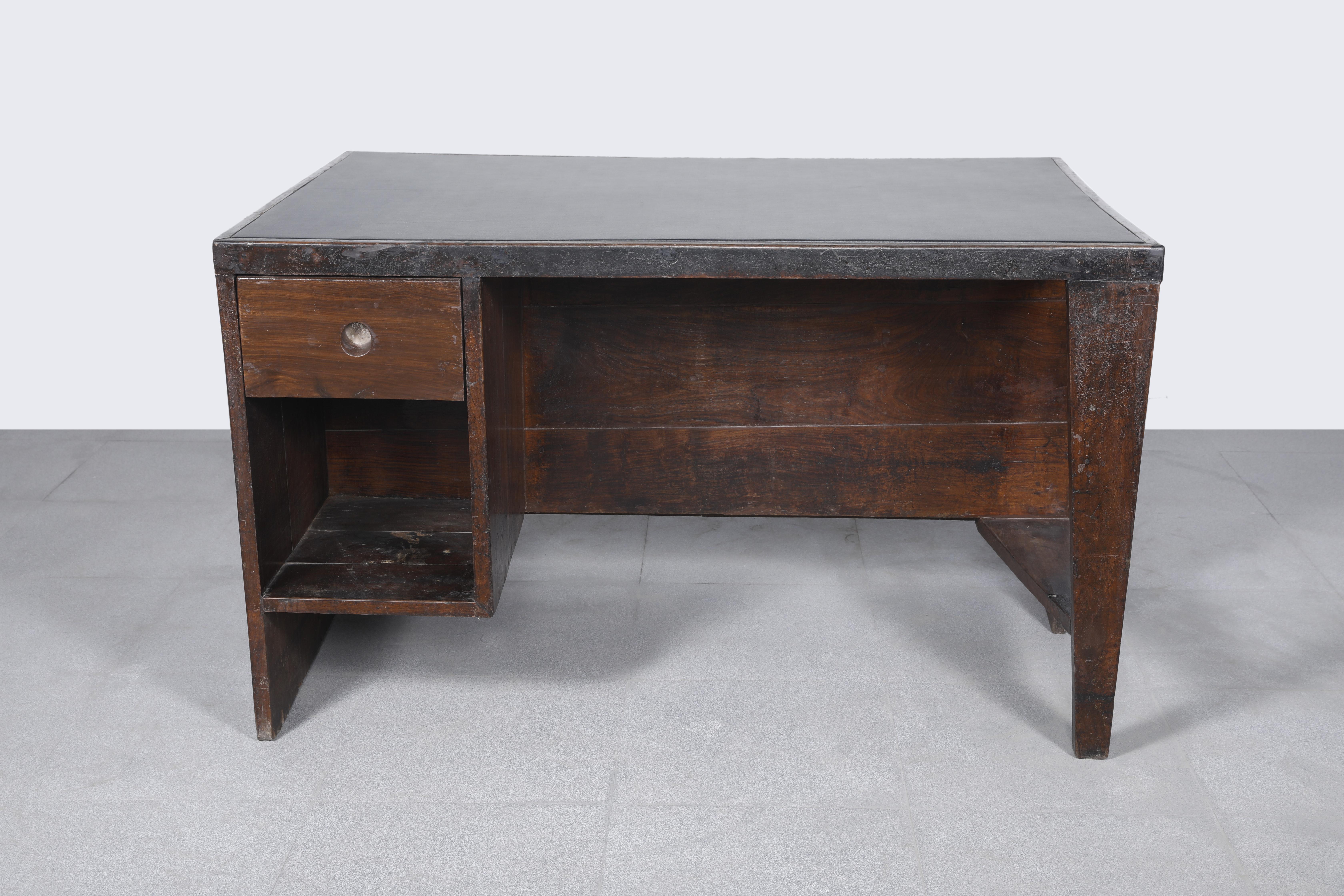 Office desk, 1957-1958. Rectangular top covered in black leather on a frame, affixed on one side by a panel forming a left side leg with a box section including a drawer and compartment and on the other side, a profiled leg with a flat triangular