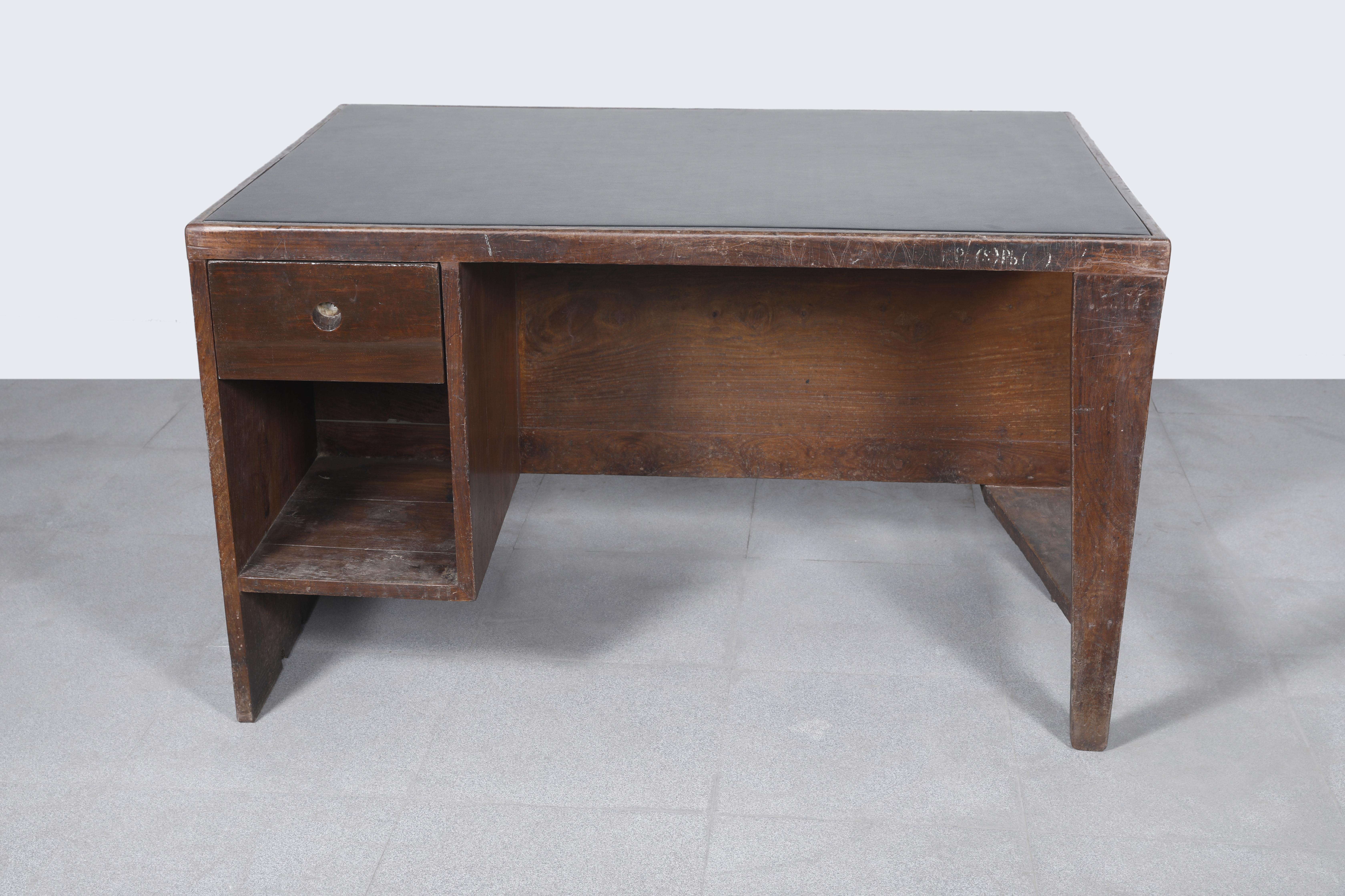 Office desk, 1957-1958. Rectangular top covered in black leather on a frame, affixed on one side by a panel forming a left side leg with a box section including a drawer and compartment and on the other side, a profiled leg with a flat triangular
