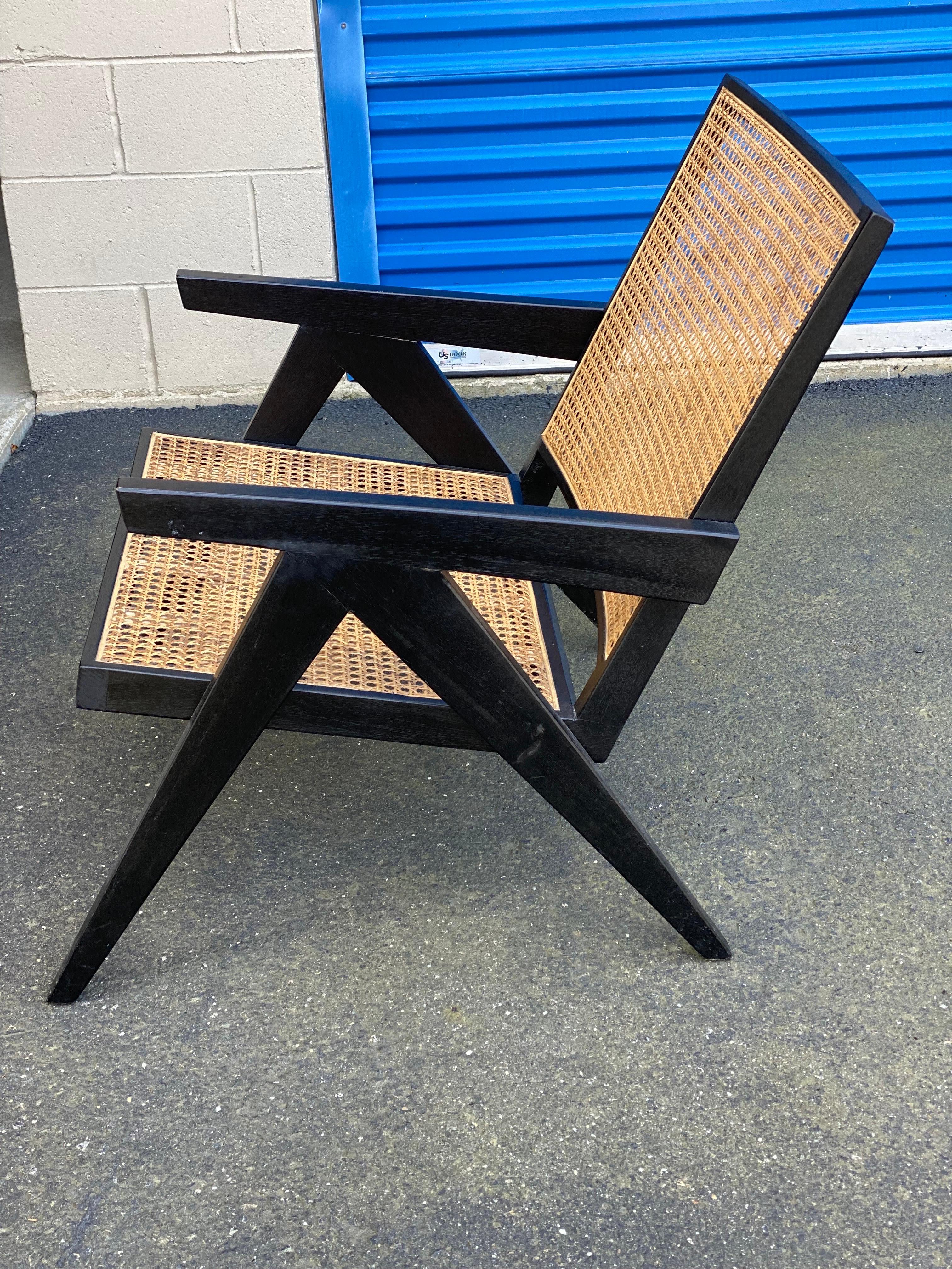 Chaise basse à accoudoirs noire de style Pierre Jeanneret
Une belle reproduction de l'emblématique Easy Chair de Pierre Jeanneret, en noir, avec assise et dossier cannés. L'assise est renforcée par une bande de rembourrage.

Condit : Légère usure,