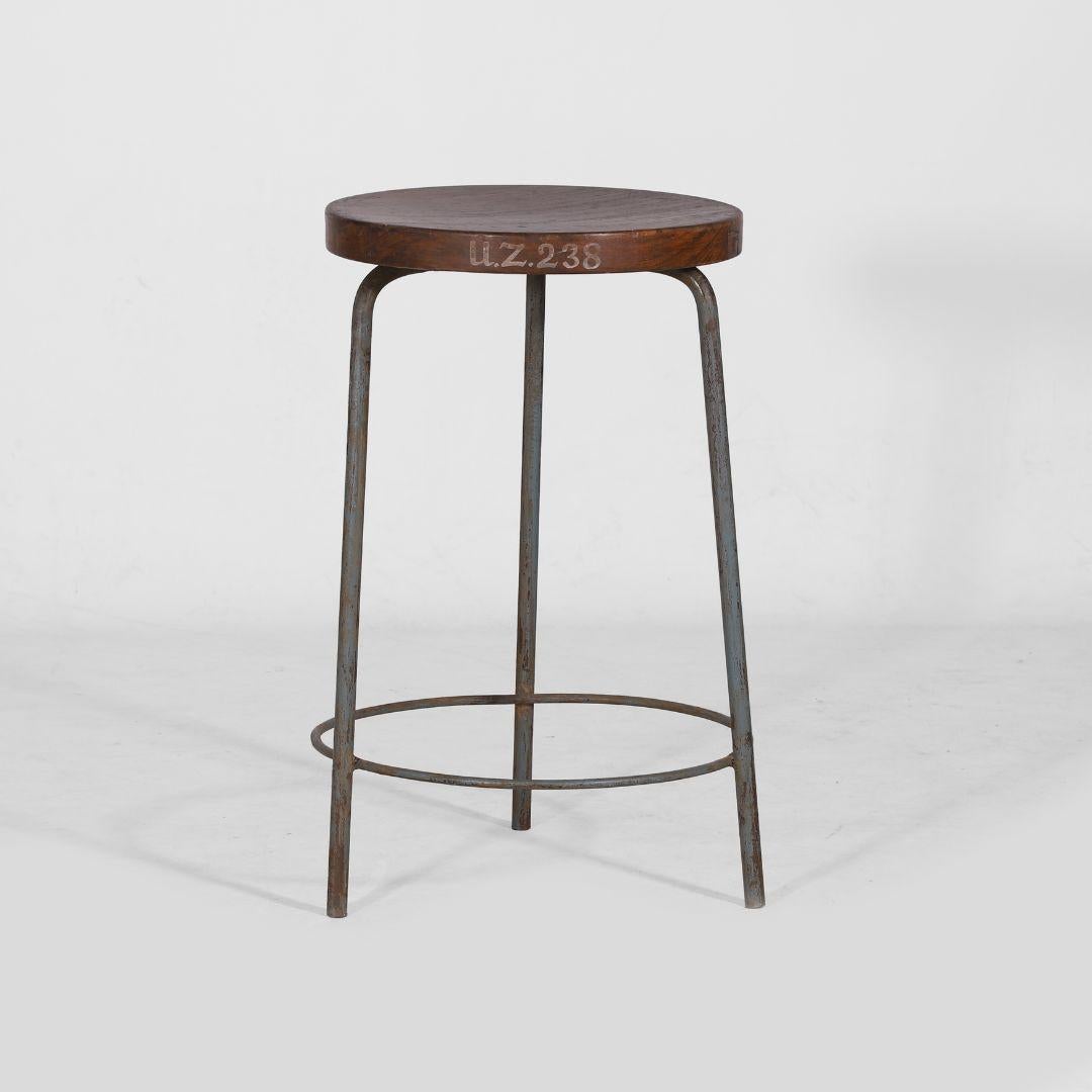 Authentischer Hocker von Pierre Jeanneret aus massivem Teakholz und geschweißtem Eisen, mit einem charakteristischen runden Dreibeinfuß und einer dezent konkaven Sitzfläche. Gestempelt mit der Kennzeichnung U.Z. 238.

- Abmessungen: Höhe 55 cm,