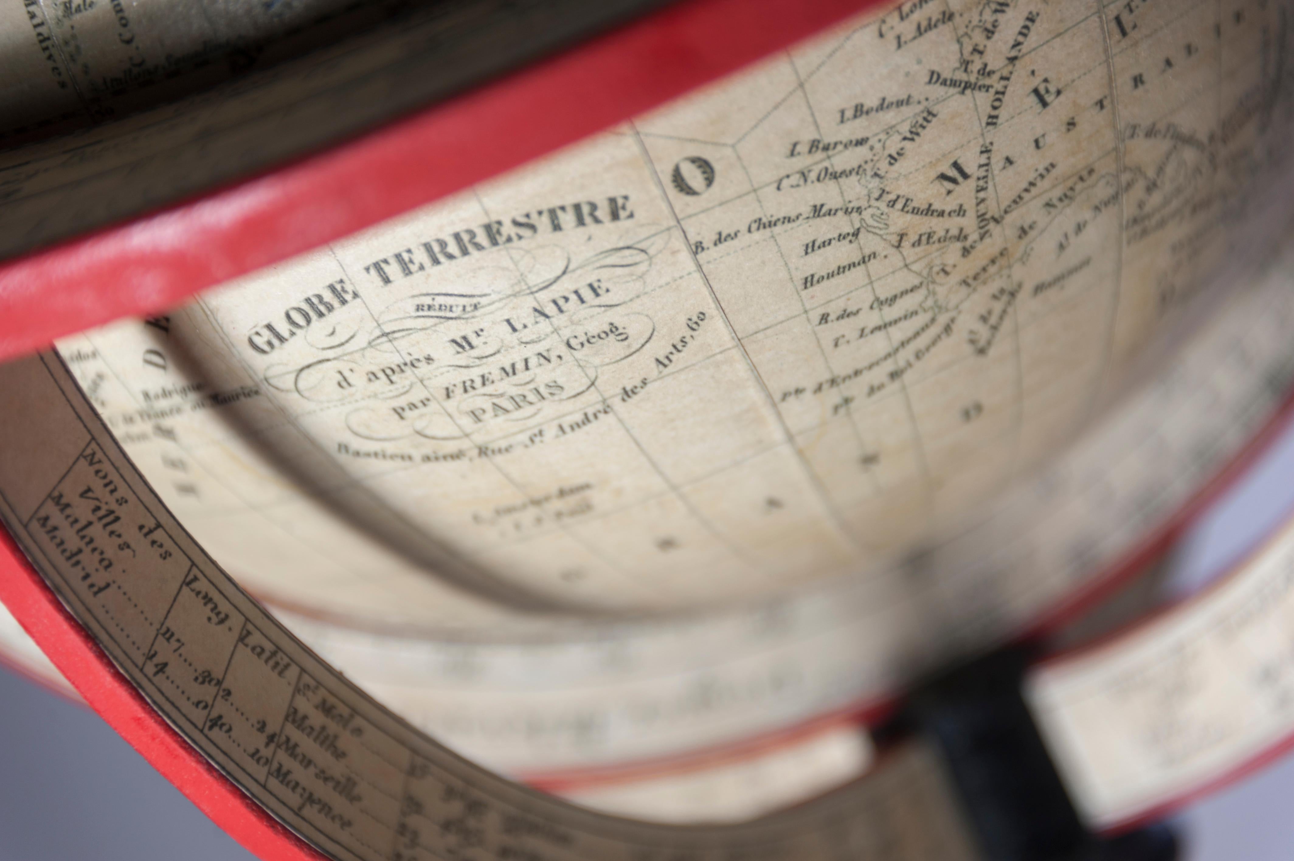 This hand coloured 9 inch terrestrial desk globe is presented on a wooden stand comprising a papered meridian ring which sits inside a horizon ring. The horizon ring is supported by four arms each showing the latitude and longitude of cities and