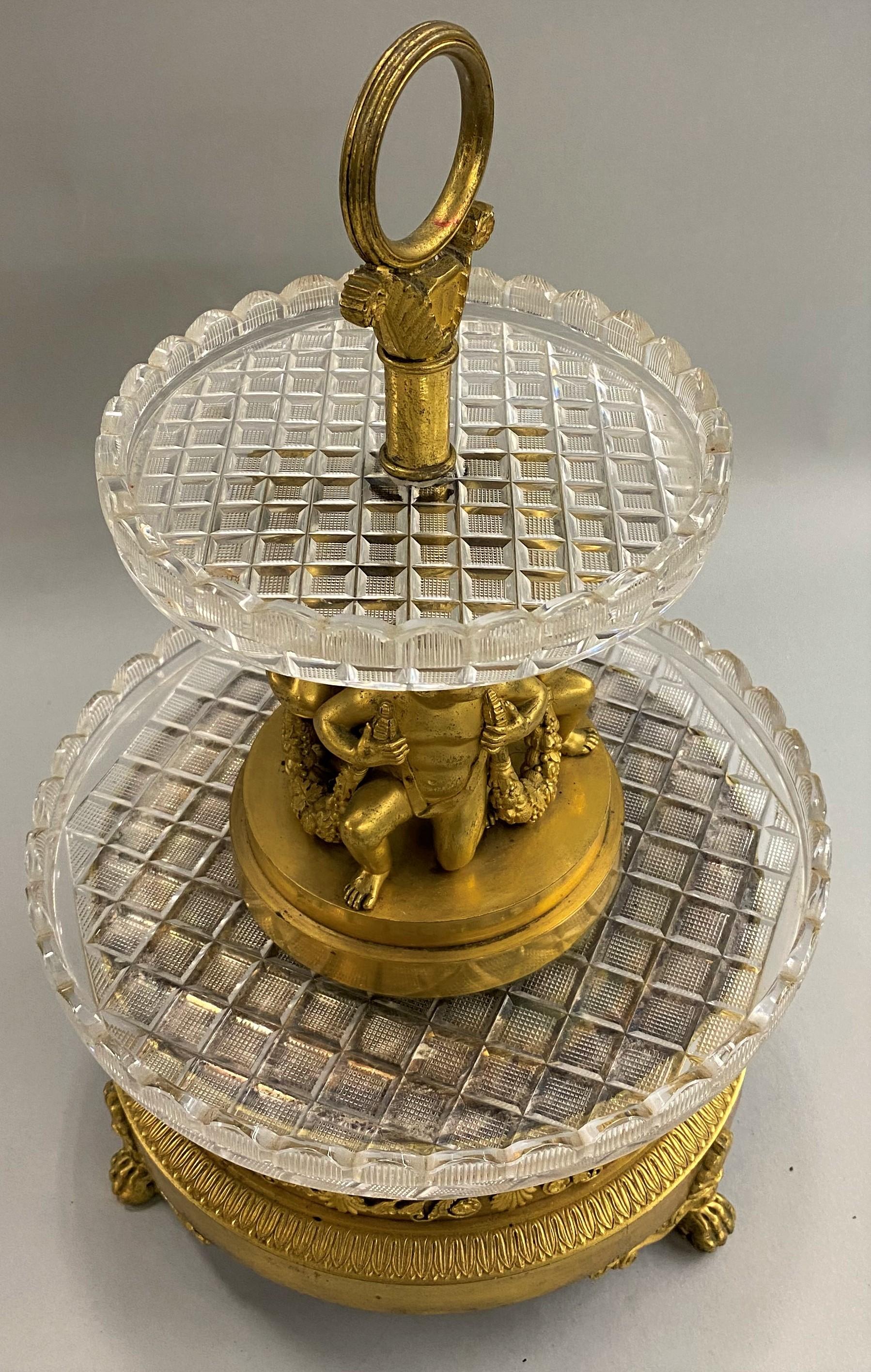 An exceptional French round centerpiece by Pierre-Phillipe Thomire (1751-1843) with tiered graduated Baccarat crystal round trays set in mercury gilt bronze with three figures holding foliate swags, supported on a round footed base with foliate and