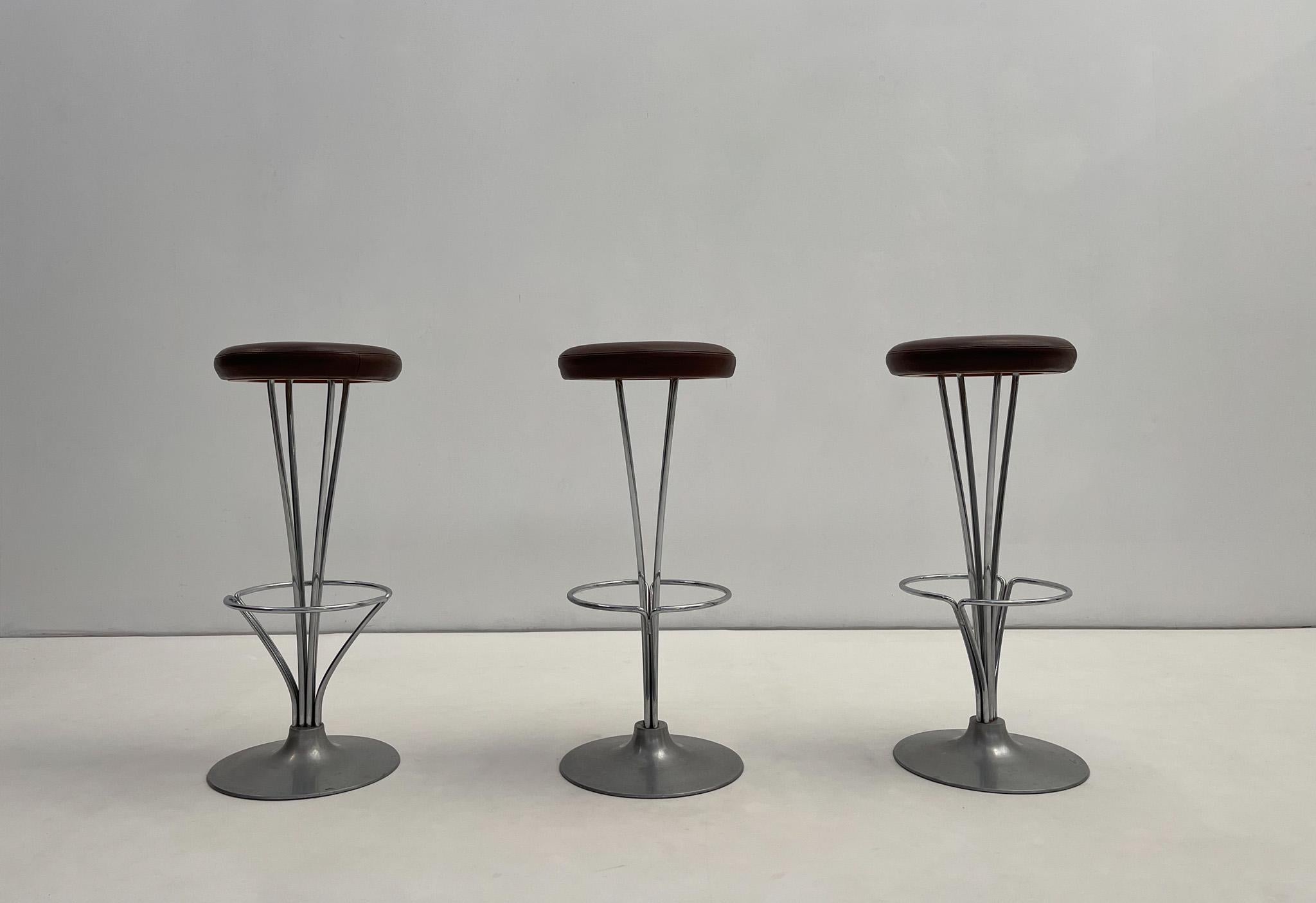 This set of three bar stools, designed by Piet Hein for Fritz Hansen, epitomizes mid-century Scandinavian elegance. Featuring their original brown leather upholstery, the seats exude a warm, vintage character that complements the sleek chrome metal