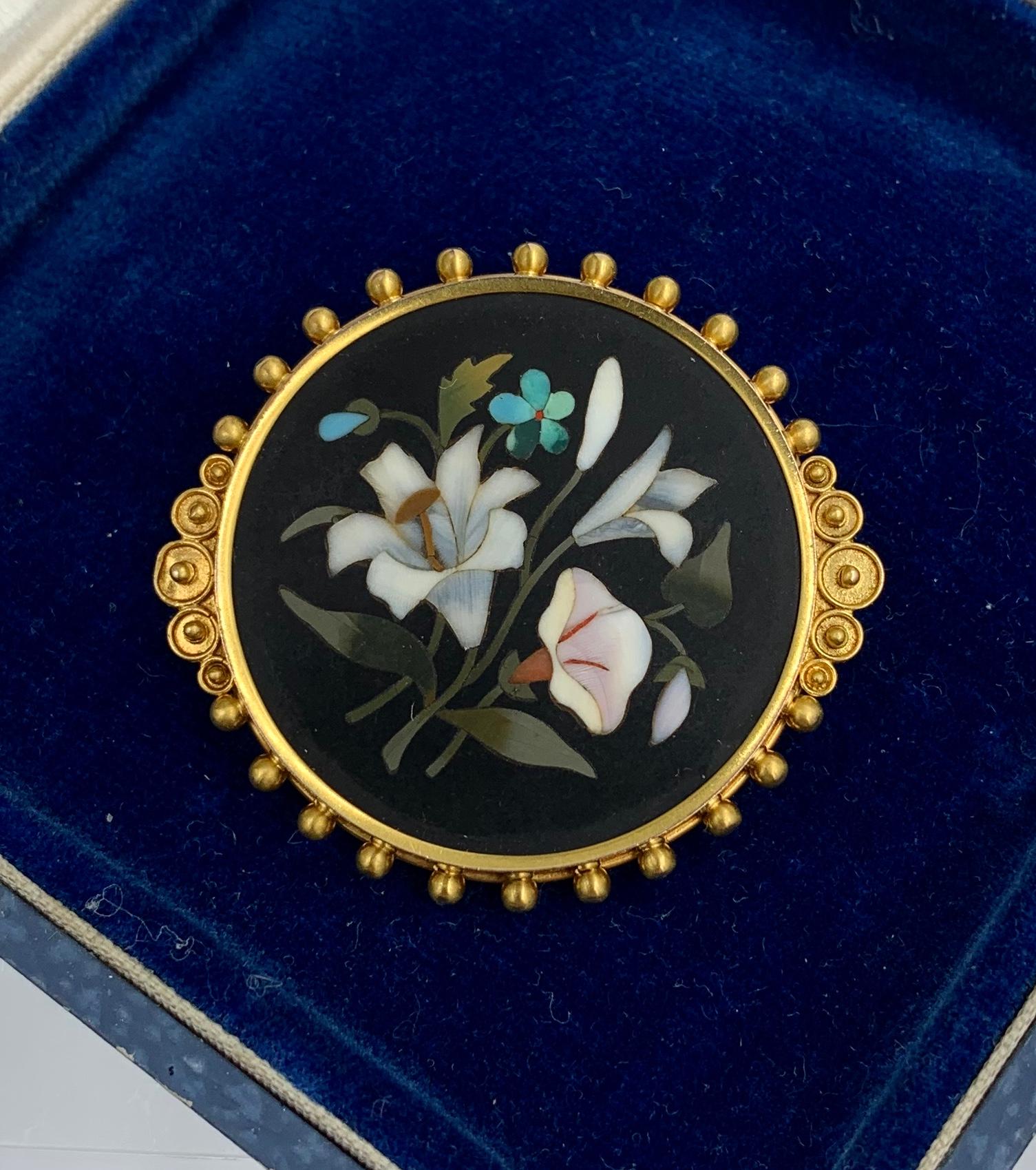 A stunning Pietra Dura Brooch with inlaid semi-precious stones creating a mosaic image of flowers including lily, poppy and forget-me-not flowers.  The brooch is a masterpiece of Pietra Dura work.  The vivid flowers and leaves set against the black