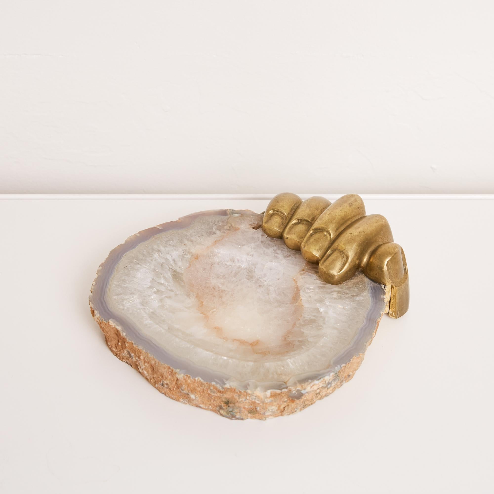 Agate tray with cast bronze hand by Italian-Brazilian artist Pietrina Checcacci. The hand carved stone bowl object features a patinated bronze hand attached to the side of the tray as if it is gripping it. The tray features a flat concave opening