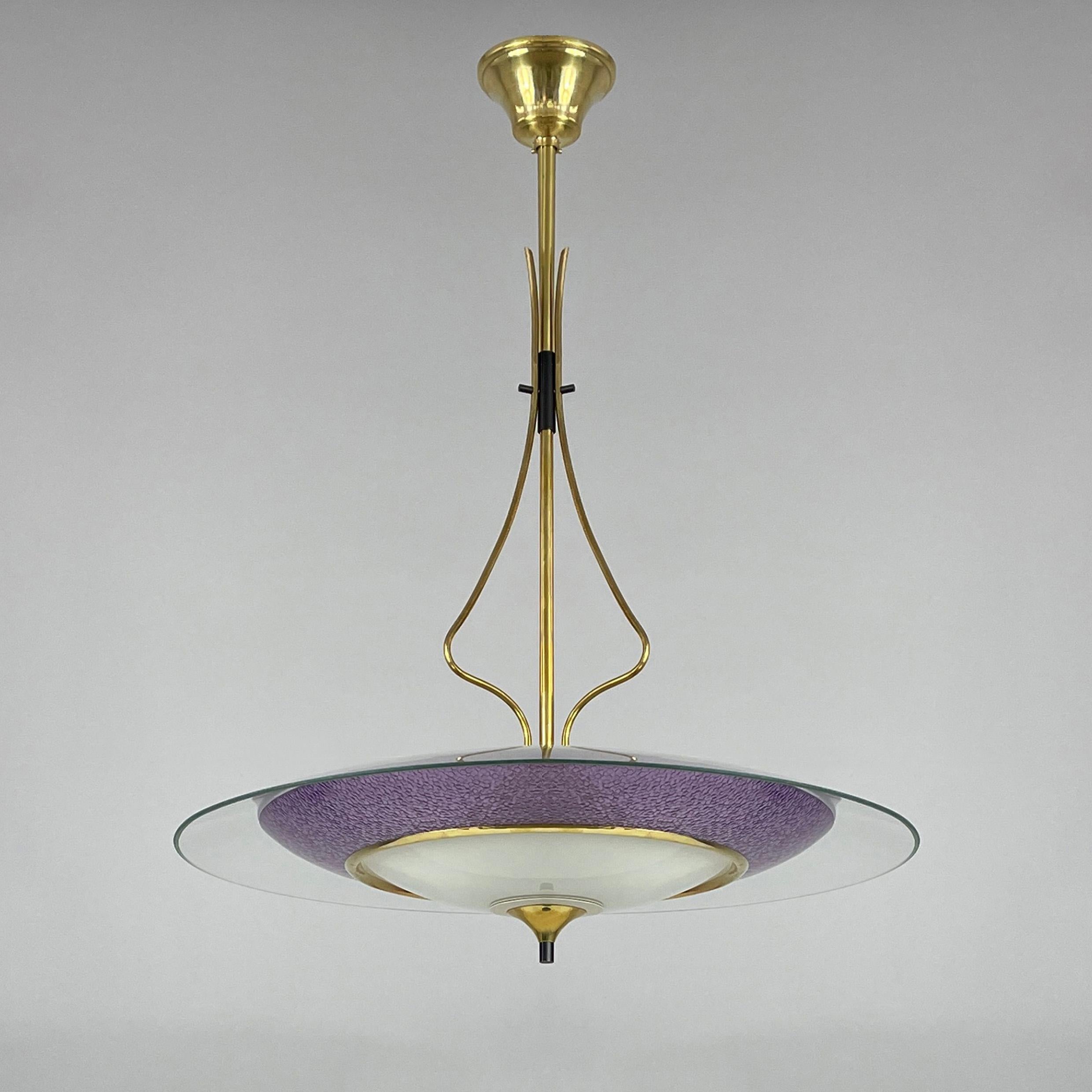 This elegant mid-century pendant was designed and manufactured in Italy in the 1950s. 

It features a brass central rod that extends into a decorative, curved structure supporting a large circular clear glass shade. The glass has a lavender 