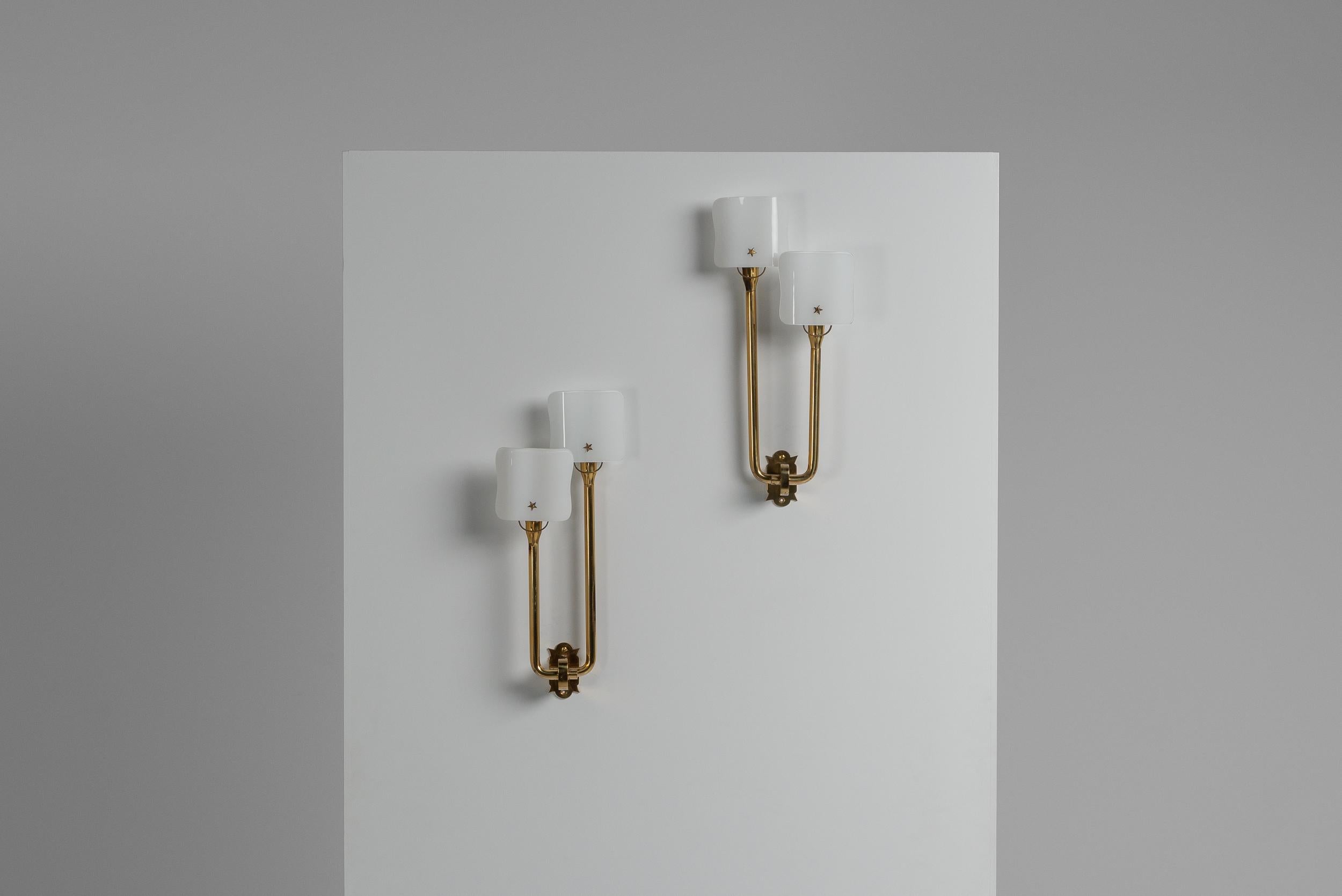 Highly rare pair of wall lamps designed by Pietro Chiesa and manufactured by Fontana Arte in Italy in 1940. These early wall lamps have a solid brass structure and milk glass shades in an abstract flower shape. A nice detail is the brass star which