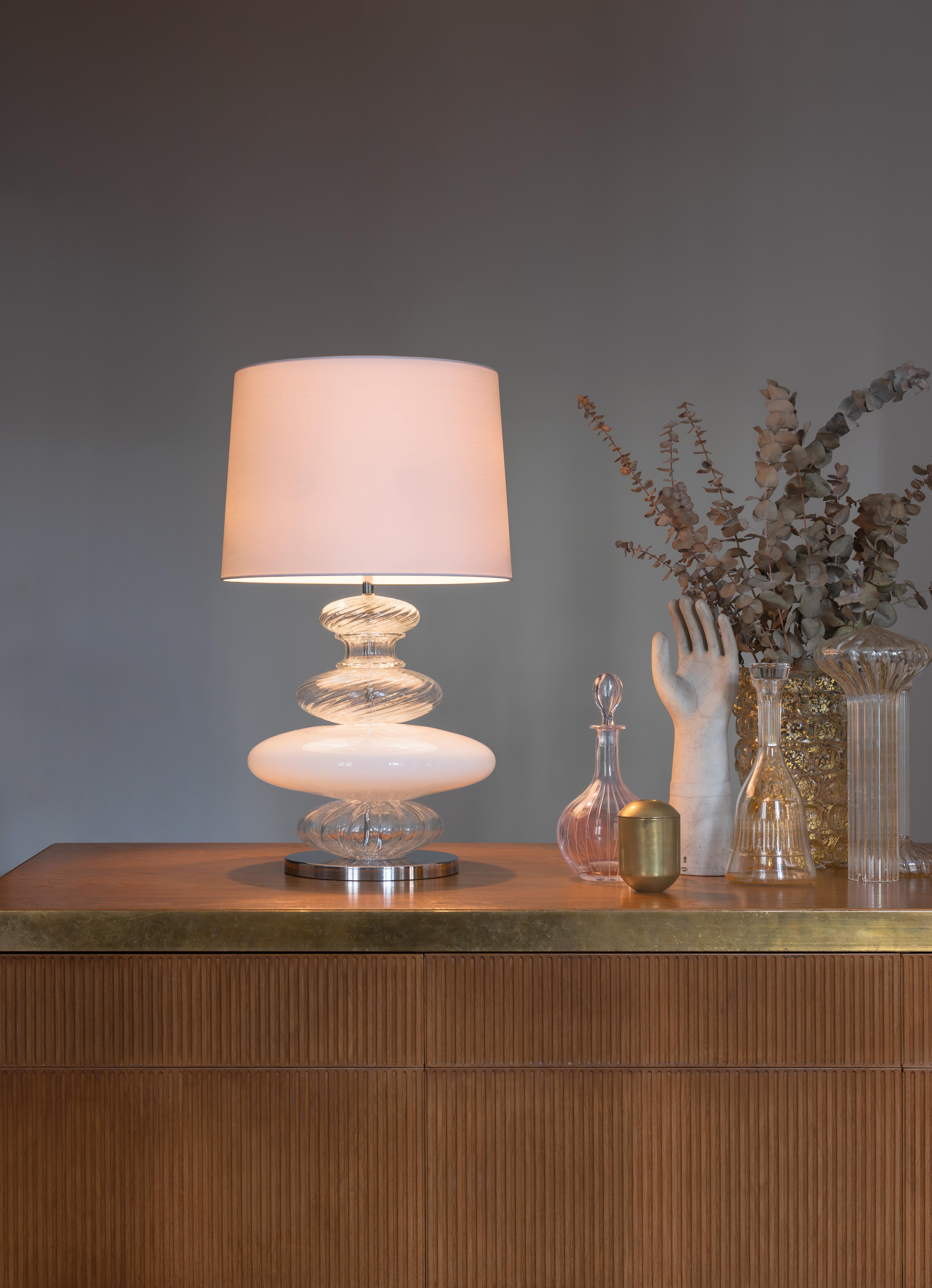 The Pigalle 5678 table lamp in white/crystal glass with a white shade, is a lamp with a lavish central body with soft-shape elements that are wrought using different techniques, on top of a chromed base. An oversized version is available. The shade