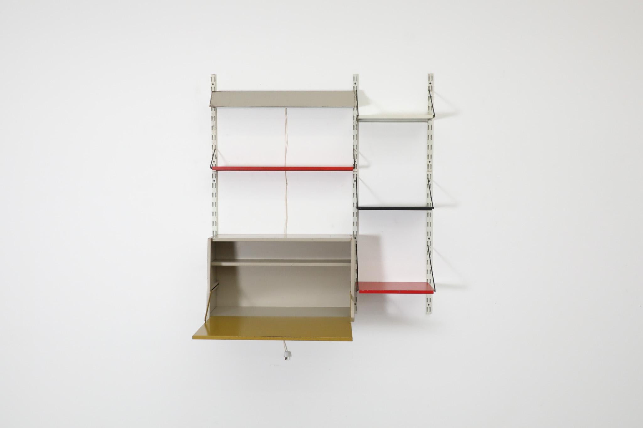 Dutch Mid-Century Pilastro enameled metal wall shelving unit. This unit features a metal drop down desk cabinet with olive green door, grey light fixture, red shelf and three mini enameled metal shelves in gray, black and red. In the 1950s and