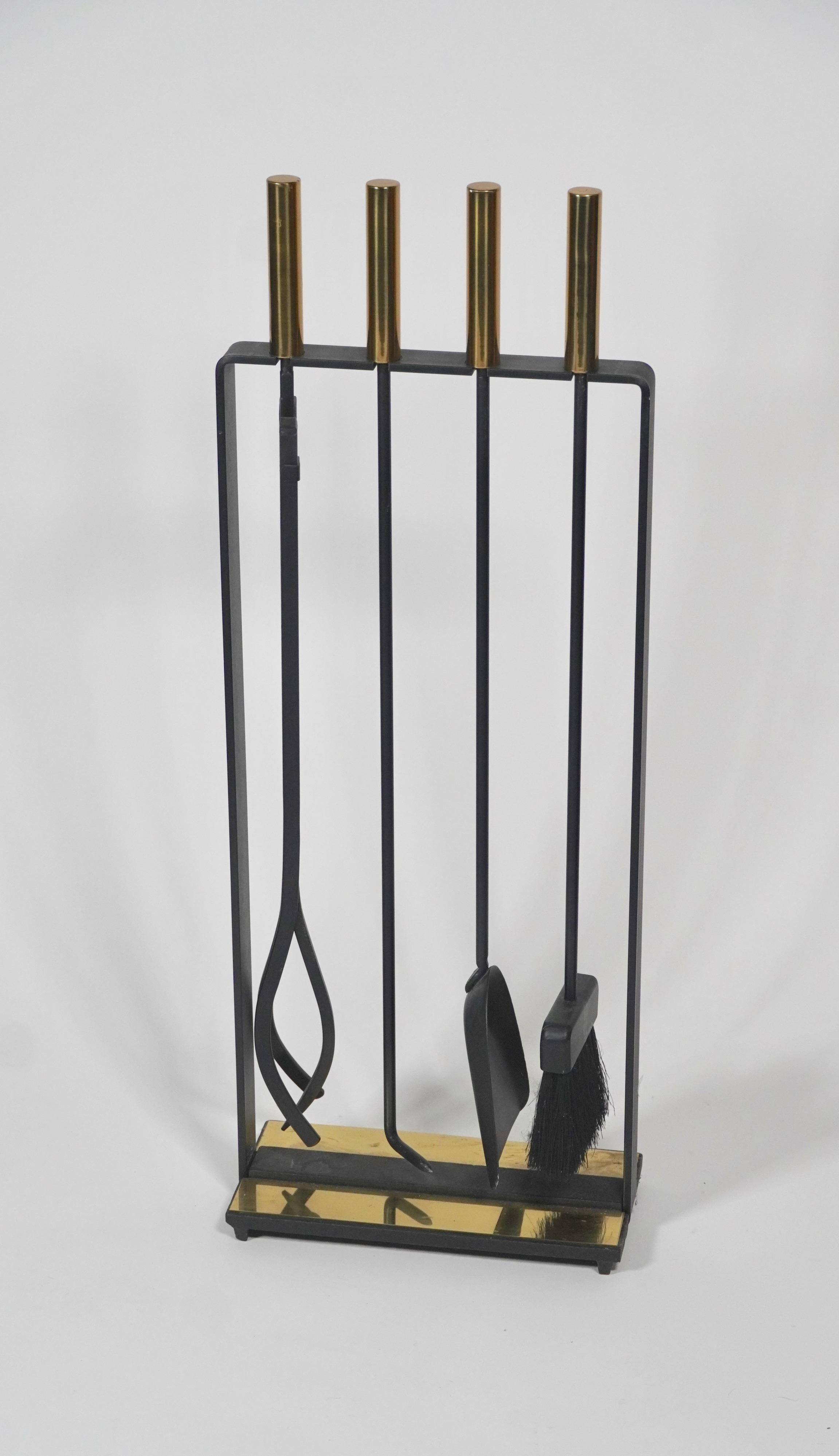 Modernist fireplace tools by Pilgrim of the United States, solid brass handles and brass base plate accent on a black cast iron and metal frame. The set includes a dust pan, brush, poker and log grabber. The brass accents are a uncommon combination