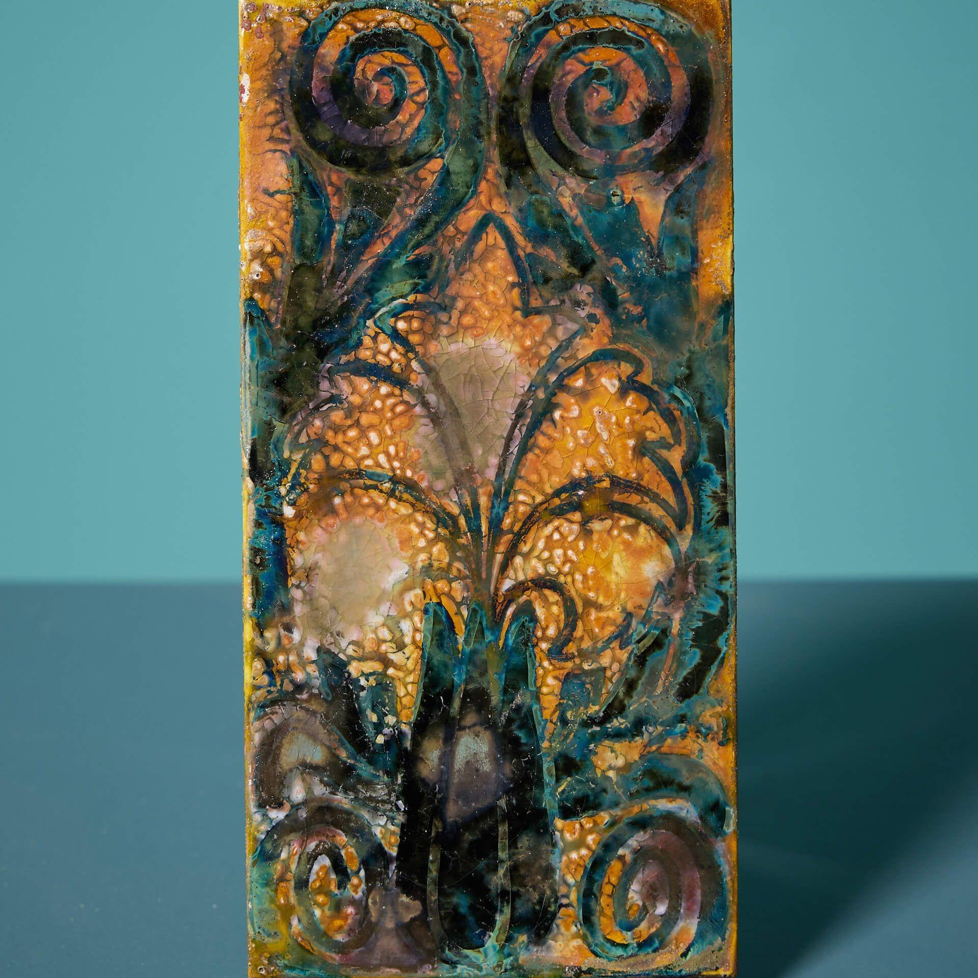 A decorative 6-inch by 3-inch Arts and Crafts lustre glaze tile by Pilkington’s Tile and Pottery Co.

Dating from the early 20th century, this antique tile is artistically decorated with a blue flower and scrolling foliage outlined in a teal glaze,
