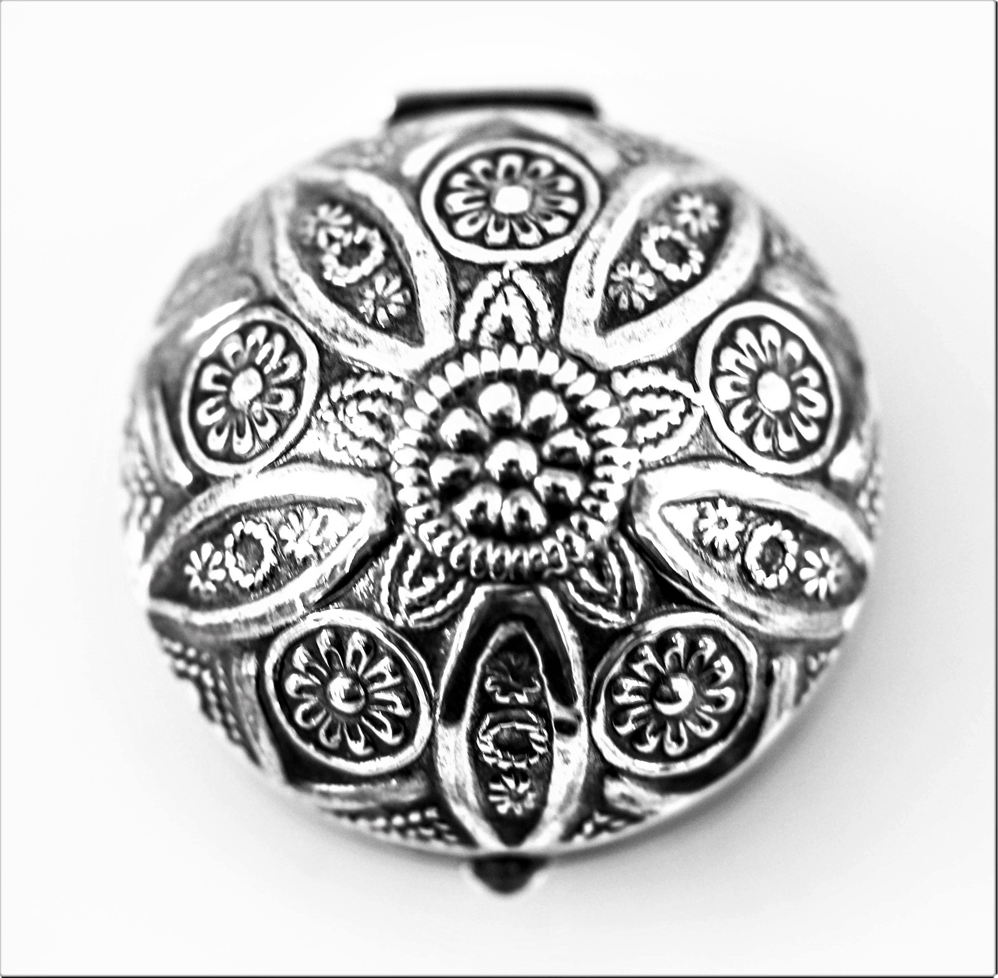 This sterling pill box is designed in a Persian style with a filigree motif. It is round on top and has a flat surface/bottom. It has a clasp on the side to open and close the lid. The lid is secured by a hinge to insure your pills stay intact. A