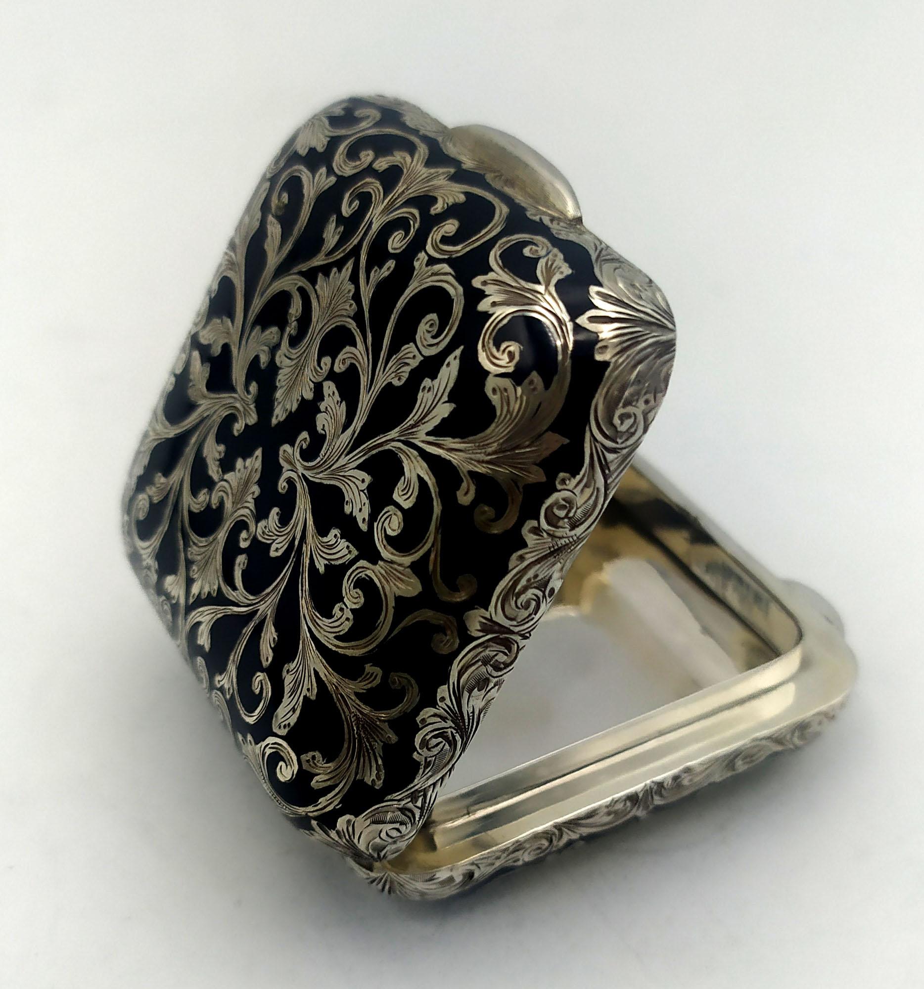 Pastillero cuadrado de ángulos redondeados y lados curvados, de plata de ley 925/1000 con un finísimo grabado a mano de estilo barroco, esmaltado al fuego con esmalte negro también en los lados. Dimensiones cm. 5 x 5 x 2. Peso gr. 85. Diseñada por