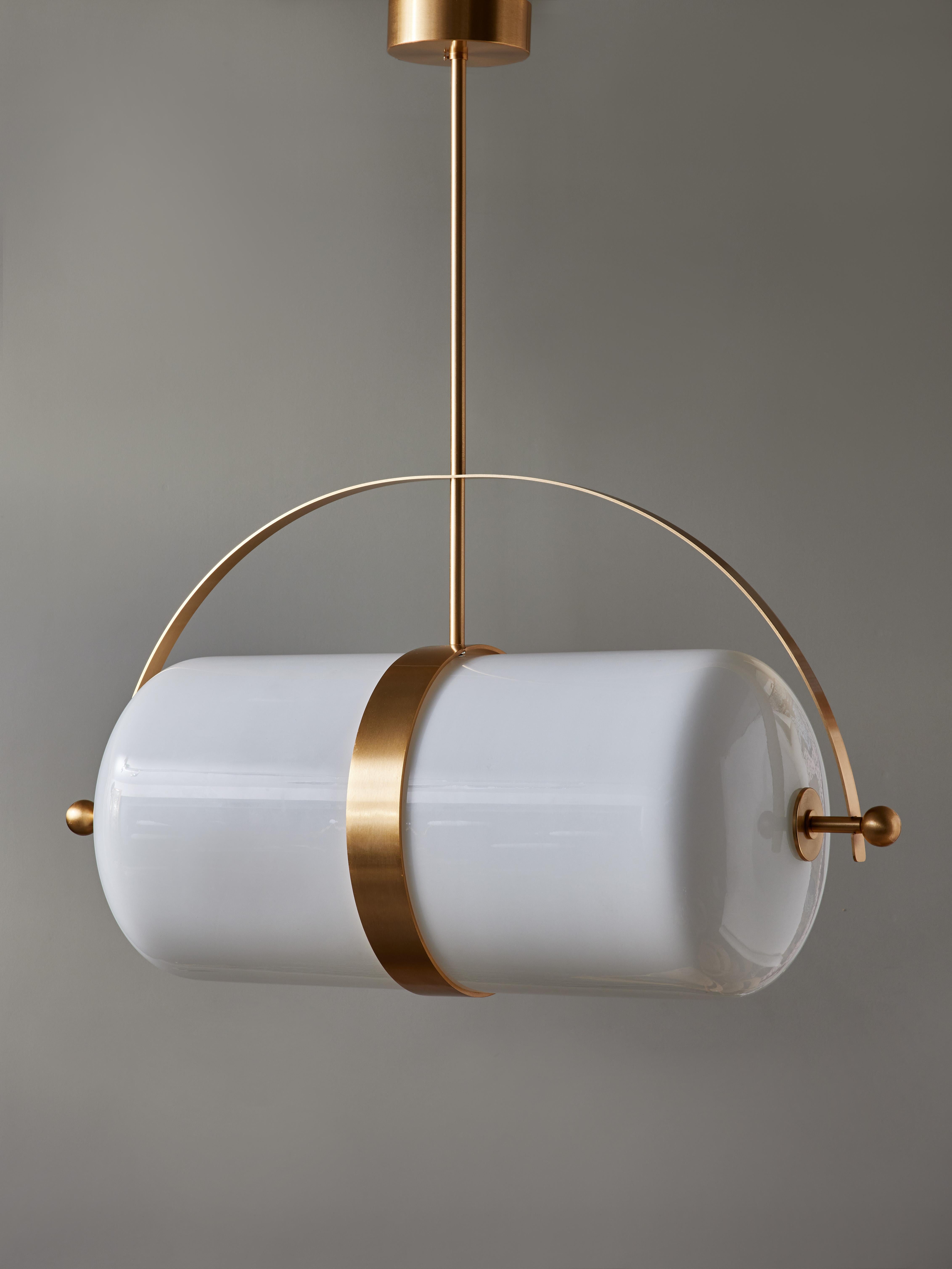 Pill shaped suspension made of two tubular opaline glass put together with a brass structure in satin finish.