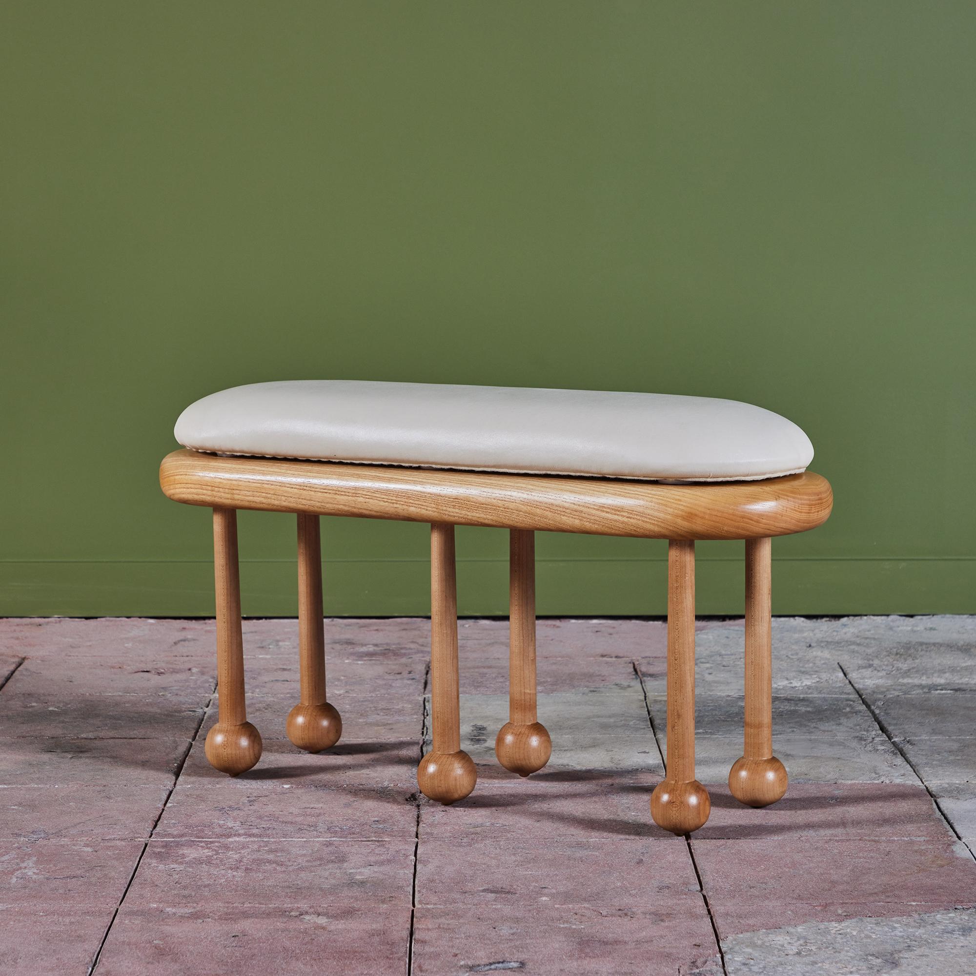 Hand crafted ash wood bench by local Los Angeles artist Evan Segota. This stool features six turned legs and an oval seat with removable Naugahyde cushion. The bottom of the cushion is felt lined and finished with brass fasteners.

Evan Segota is a