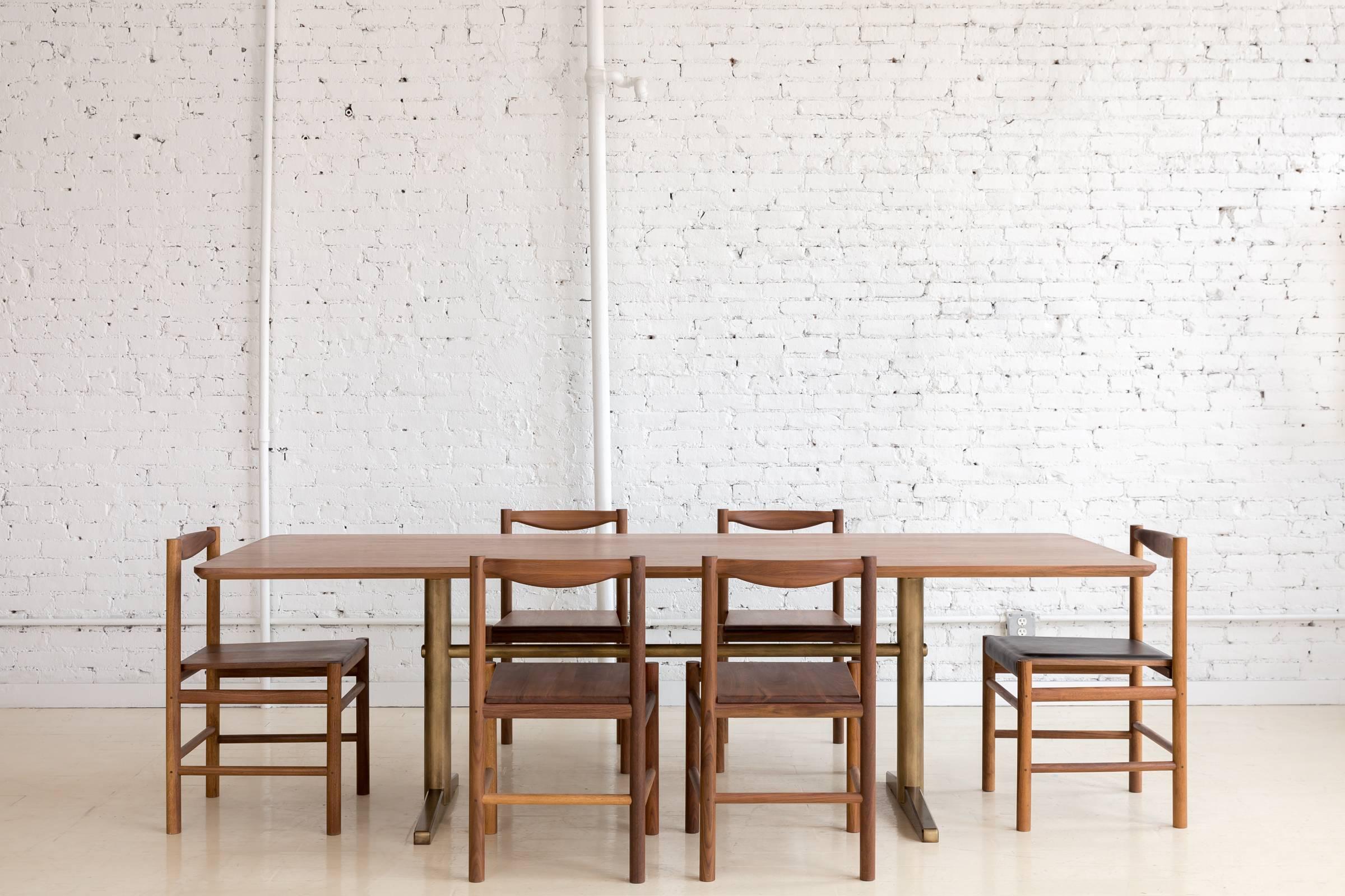 This contemporary dining table features a hardwood walnut top with rounded corners and a continuous bottom bevel that compliments details found on the brass pedestal base. 

All base components are precision machined from steel and plated in brass