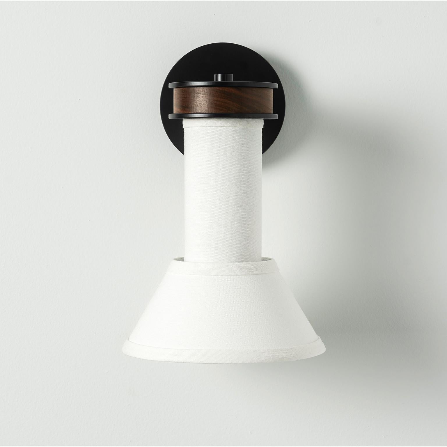 Our modern wall sconce combines symmetry and candle-like geometry to create a striking silhouette suitable for a variety of environments. A narrow shade and single column of luxurious linen descends from a curved hardwood base casting a tranquil