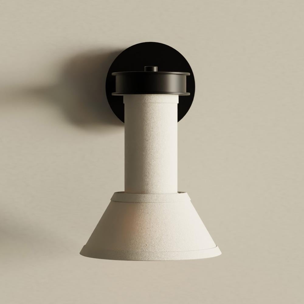 Our modern wall sconce combines symmetry and candle-like geometry to create a striking silhouette suitable for a variety of environments. A narrow shade and single column of luxurious linen descends from a curved hardwood base casting a tranquil