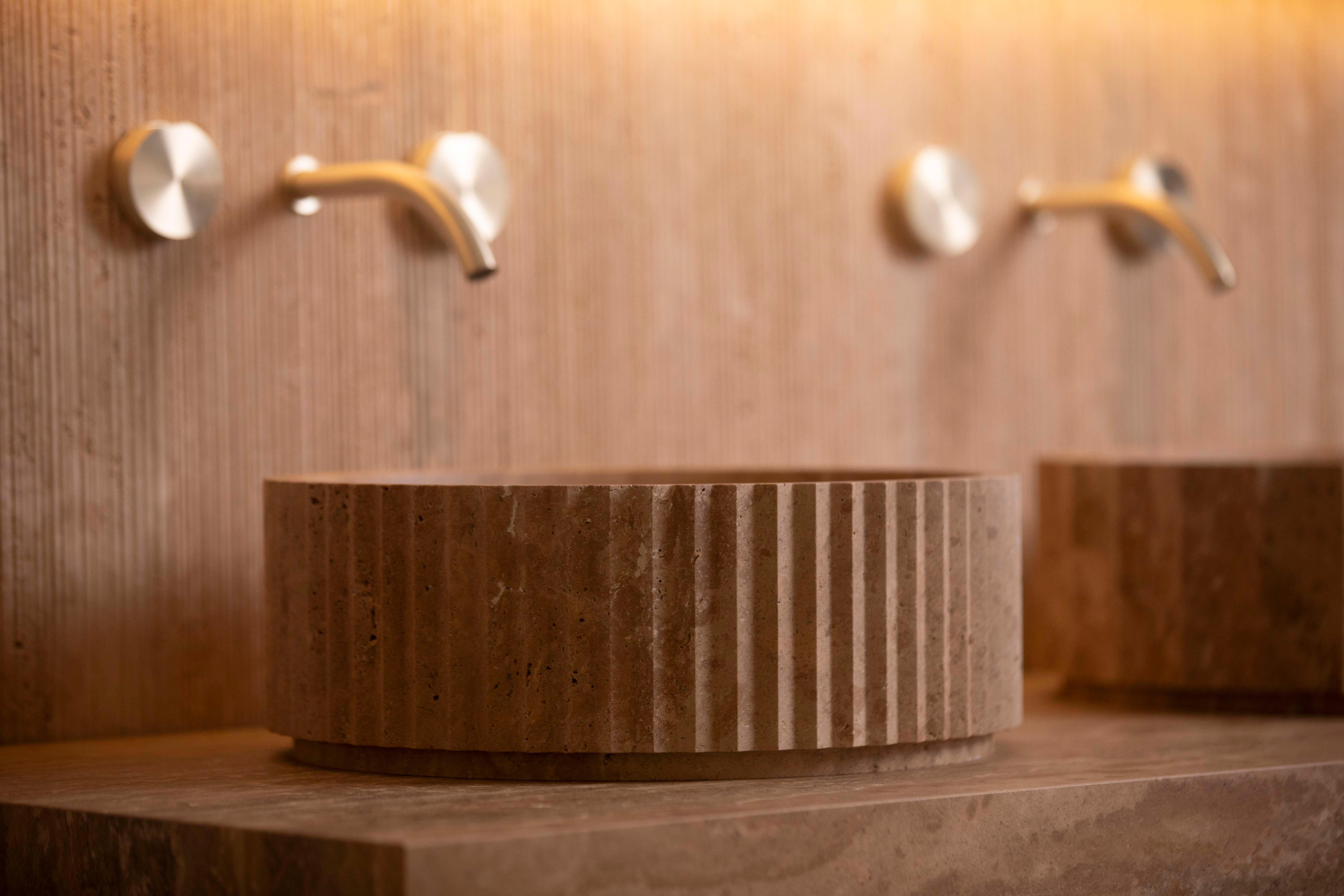 This countertop washbasin in Almond Travertine, treated with Acid Shield for enhanced protection and durability, is crafted by the renowned Italian maker Piba Marmi. A striking example of contemporary design with natural and industrial influences,