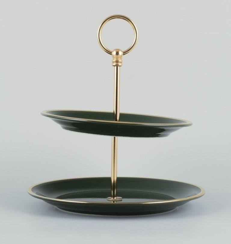 Pillivuyt, France. Cake stand/etagère in porcelain.
“Green Bistro”. Dark green glaze with gold decoration. 
Brass handle.
Circa 1970s.
Marked.
Perfect condition.
Dimensions: Diameter 23.0 cm. x Height 25.5 cm.