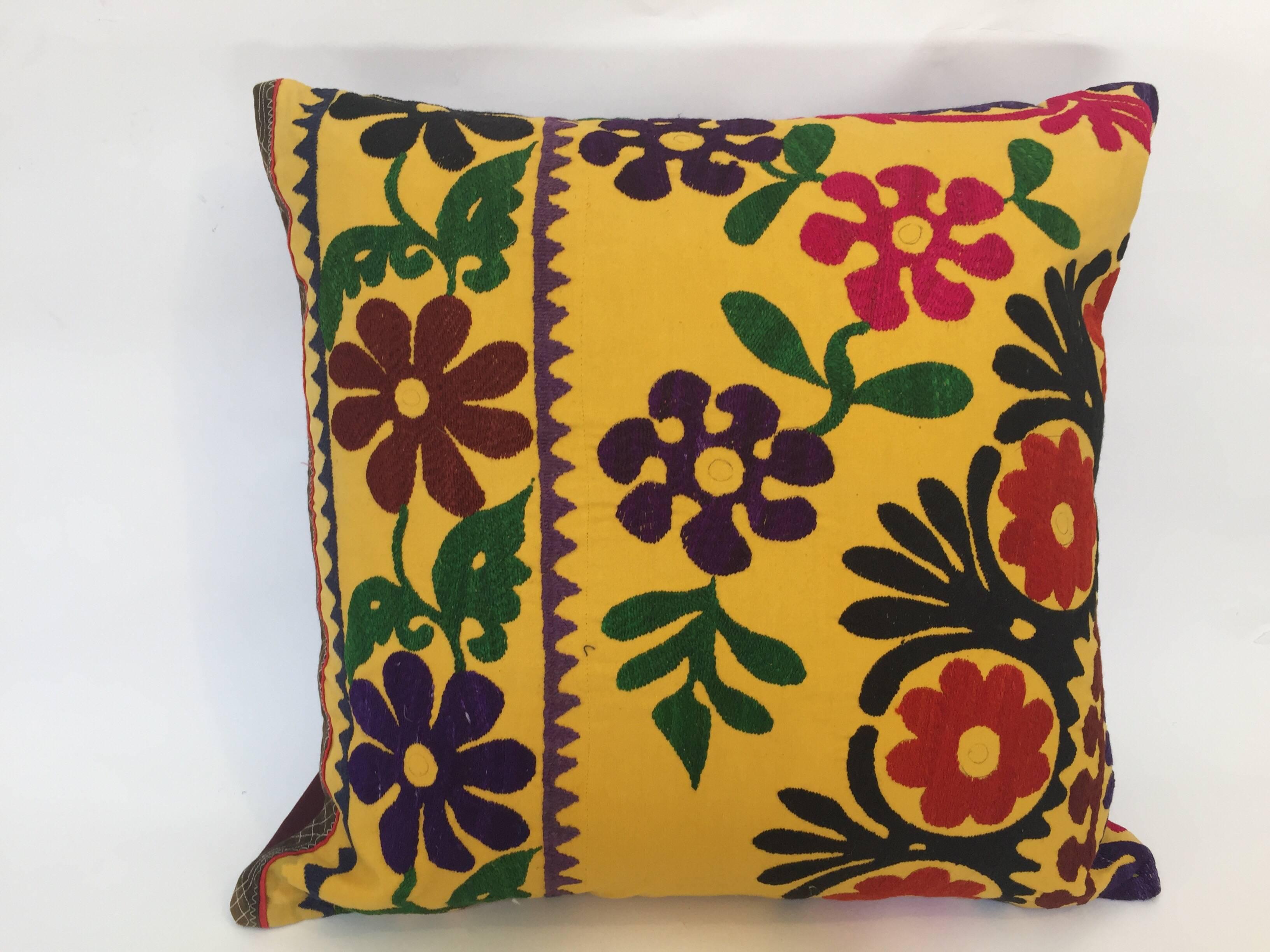 Large vintage colorful Suzani embroidery throw pillow red with colorful threads.
A yellow embroidered pillow with flower motifs in shades of black, red, yellow, purple, green magenta, with linen backing and zipper in the back.
The pillow is made