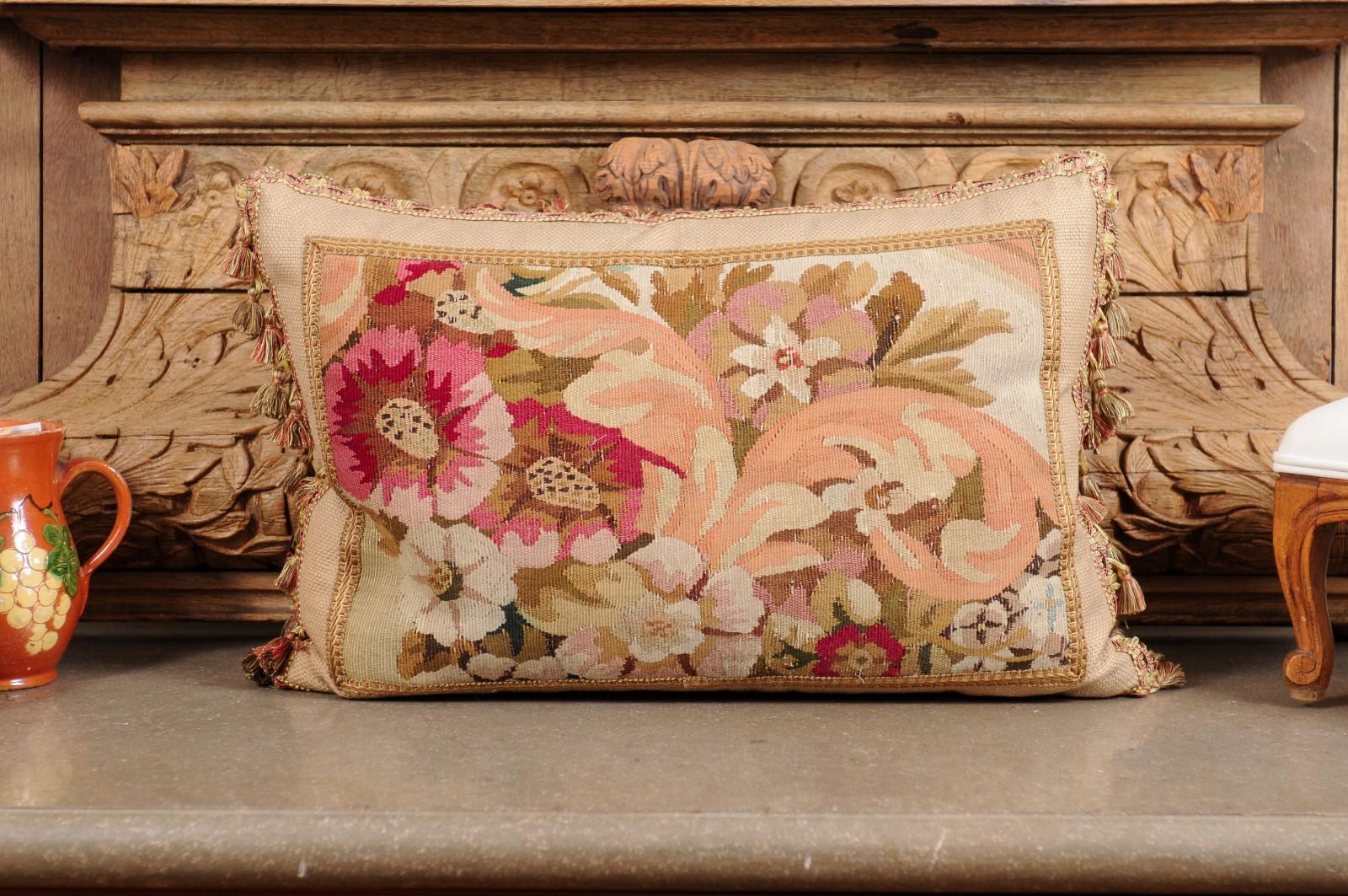 A pillow made from 19th century French tapestry, with floral decor and tassels. Crafted from a tapestry woven during the 19th century, this horizontal pillow is adorned with an abundant decor of pink and white flowers accented with green, brown and
