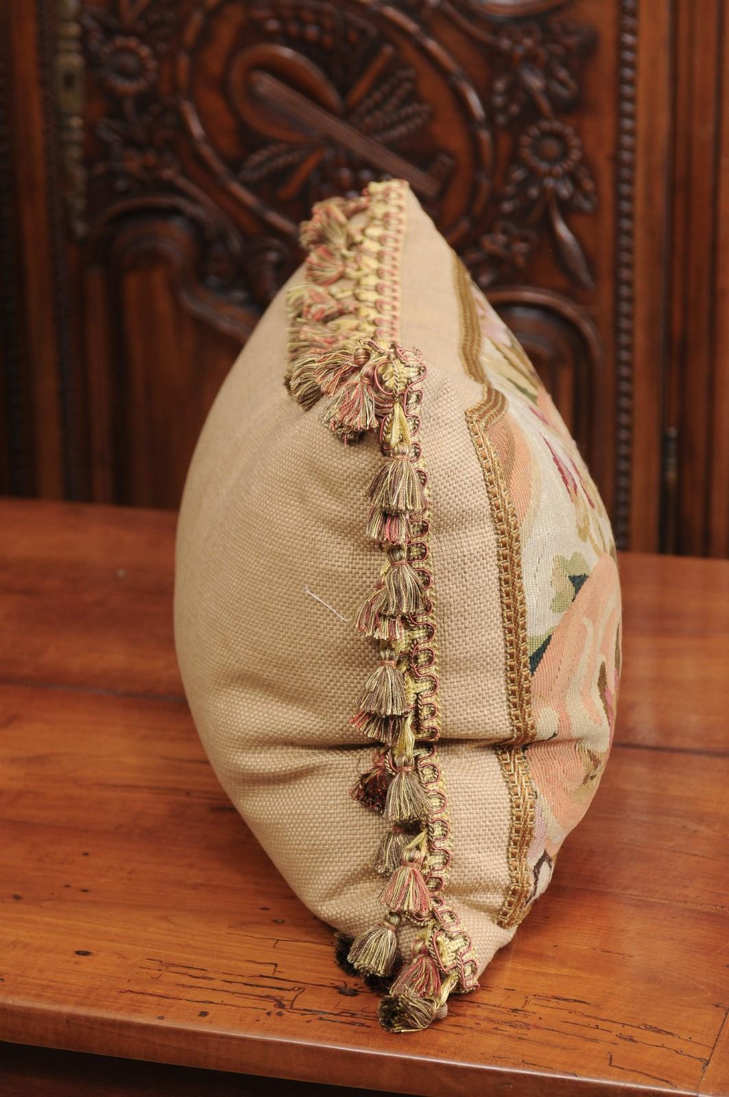 A pillow made from 19th century French tapestry, with floral decor and tassels. Crafted from a tapestry woven during the 19th century, this horizontal pillow is adorned with an abundant decor of pink and white flowers accented with green, brown and