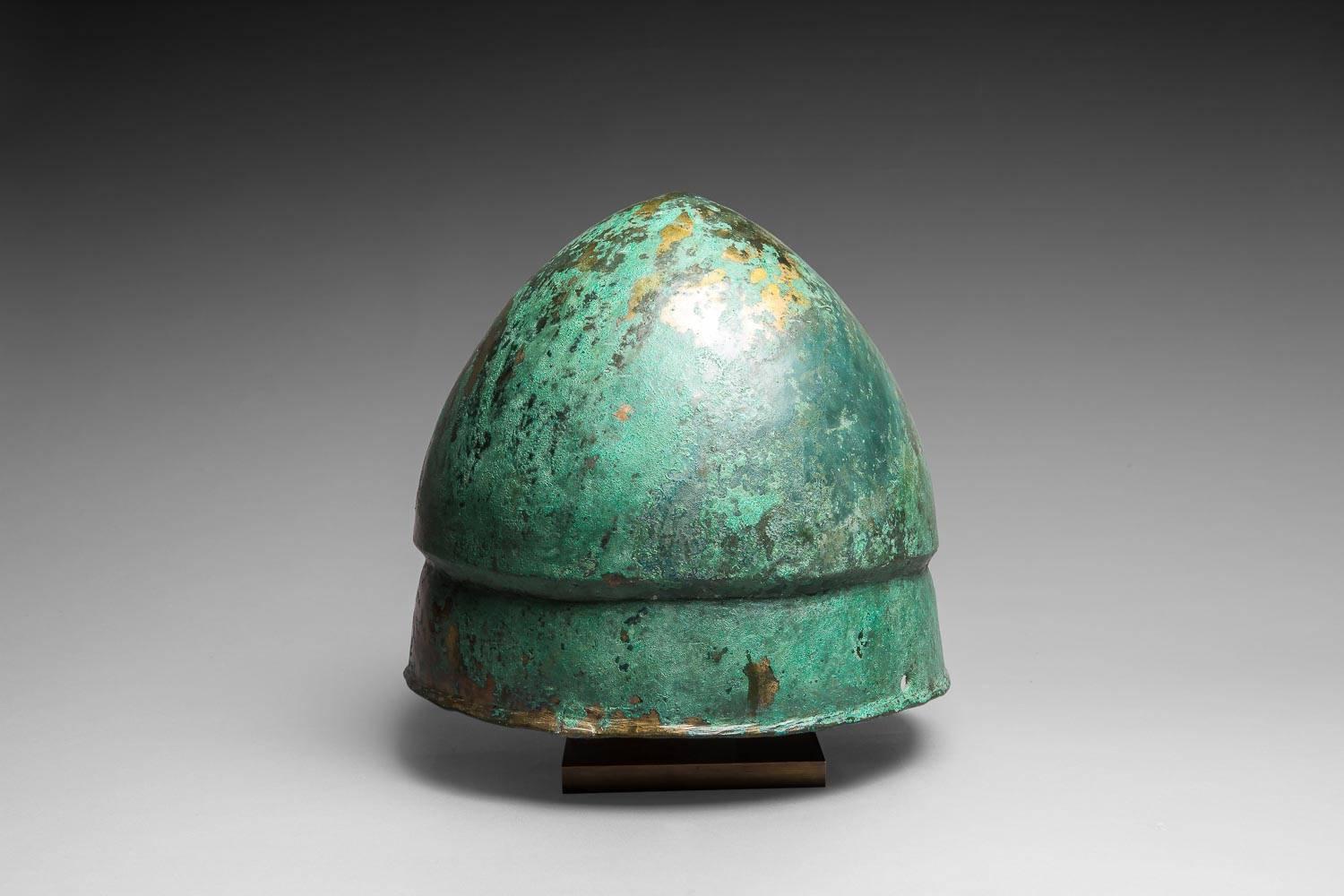 Pilos type helmet
Greek Art, 6th century BC.
Bronze.

Measures: Height: 20.2 cm; Diameter: 22 cm.

Provenance : Private collection of Mr. G.G., Paris, acquired in 2006;
Sale Hermann Historica 2006;
Former Belgian collection before