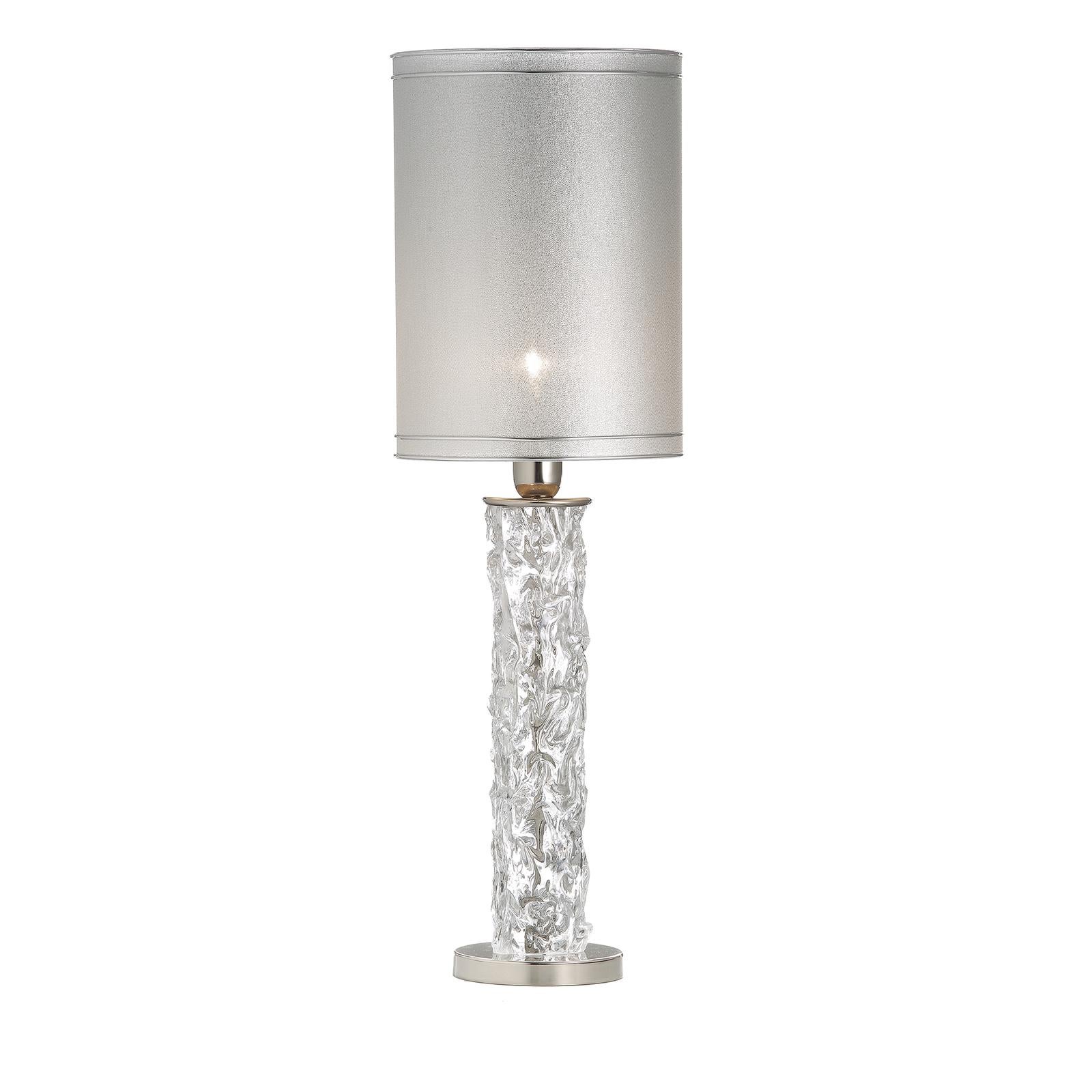 This stunning table lamp is an exquisite example of masterful craftsmanship combined with a contemporary aesthetic. Resting on a metal base with a polished nickel finish, the body of the lamp is made of transparent Murano glass shaped with several