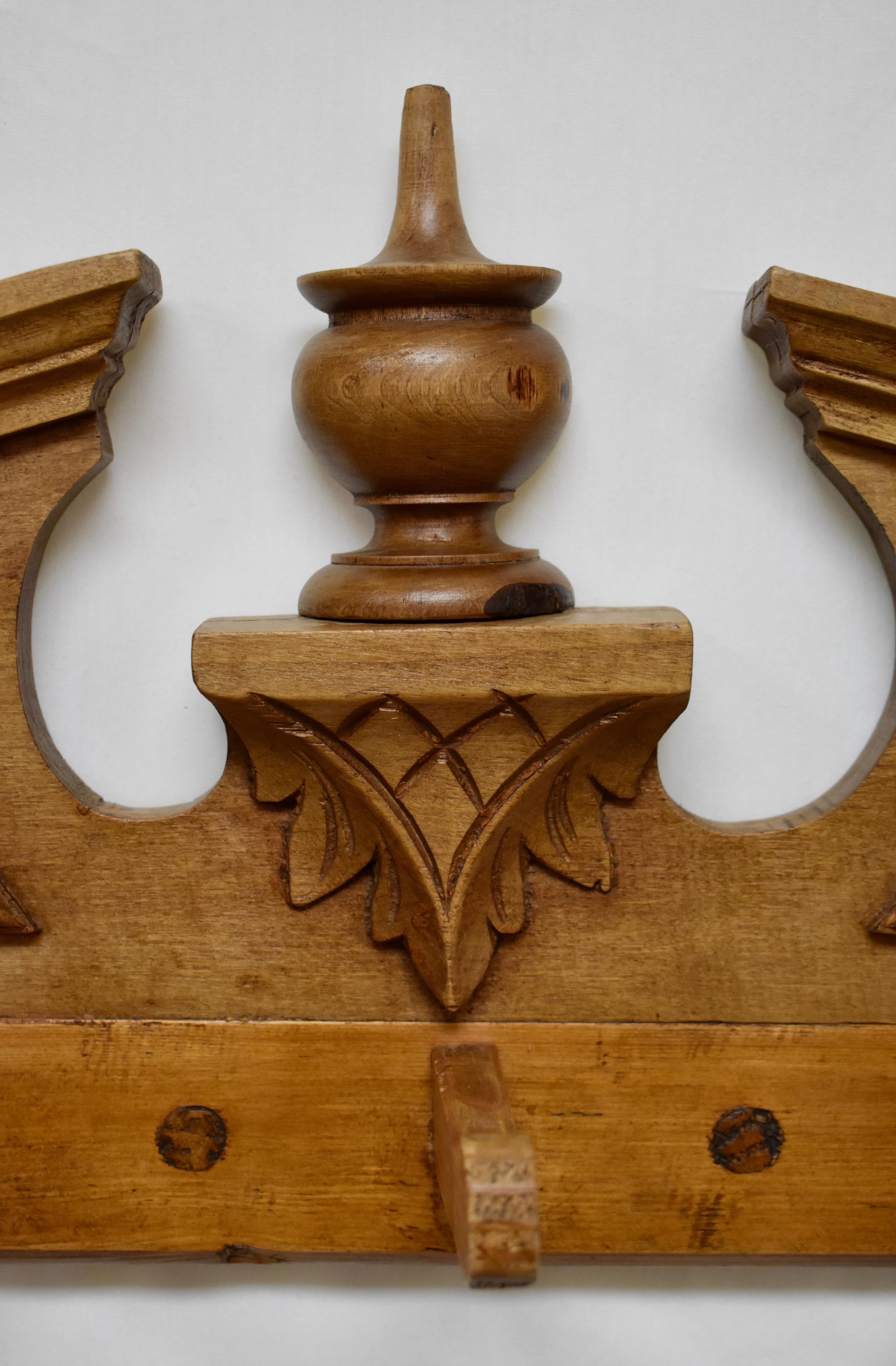 In a creative example of re-purposing, an orphan crest from the crown of an antique pine armoire, with its broken pediment and half-turned finial, has been married to a row of seven hand carved pegs from its interior. The result is this handsome and