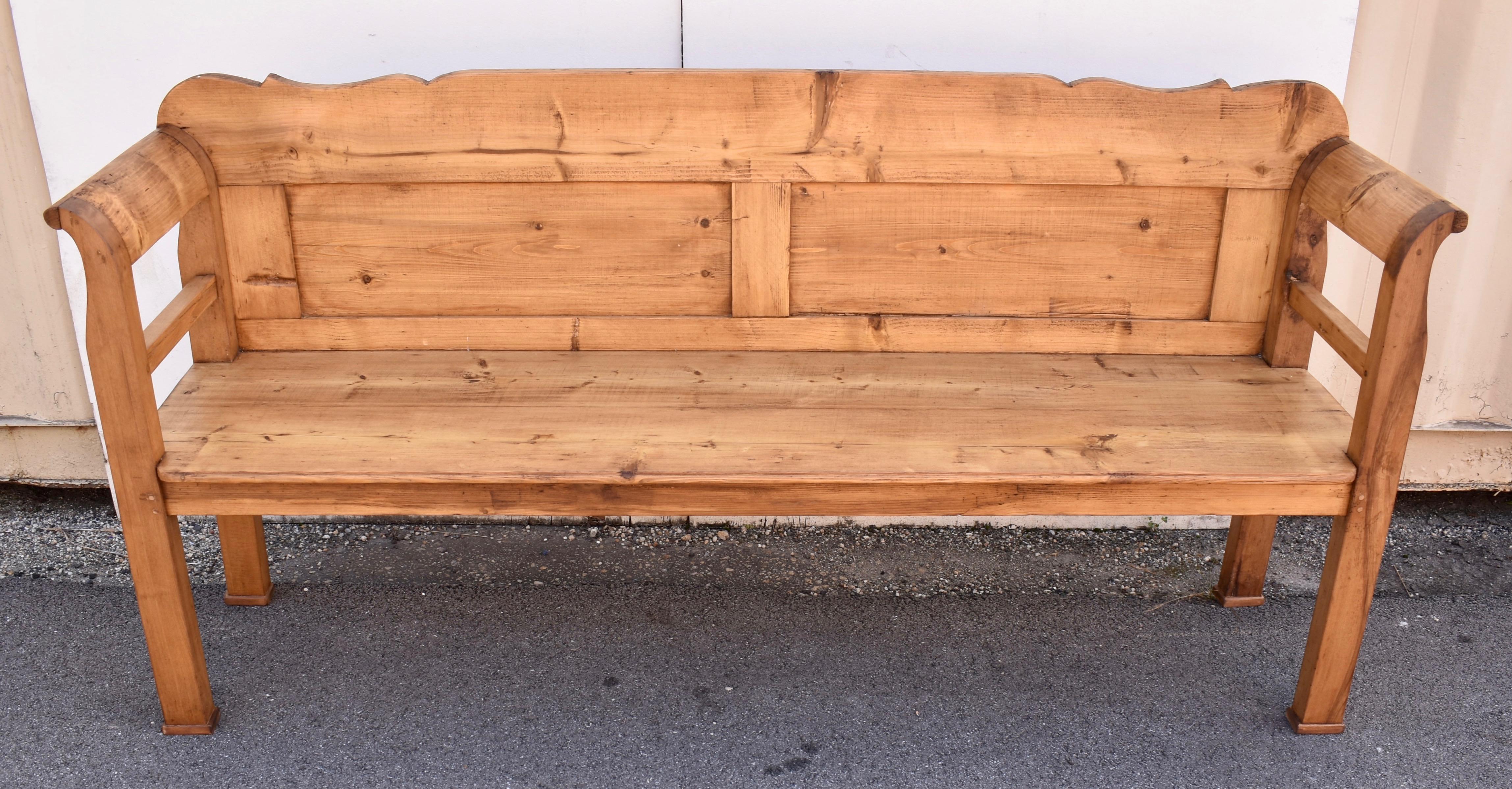 Less shapely than some of its counterparts, this bench has a long flat back rail with a short scalloped area at each end, sitting above two rectangular flat panels.  The integral legs and arms, fashioned in oak, are also mostly straight verticals,