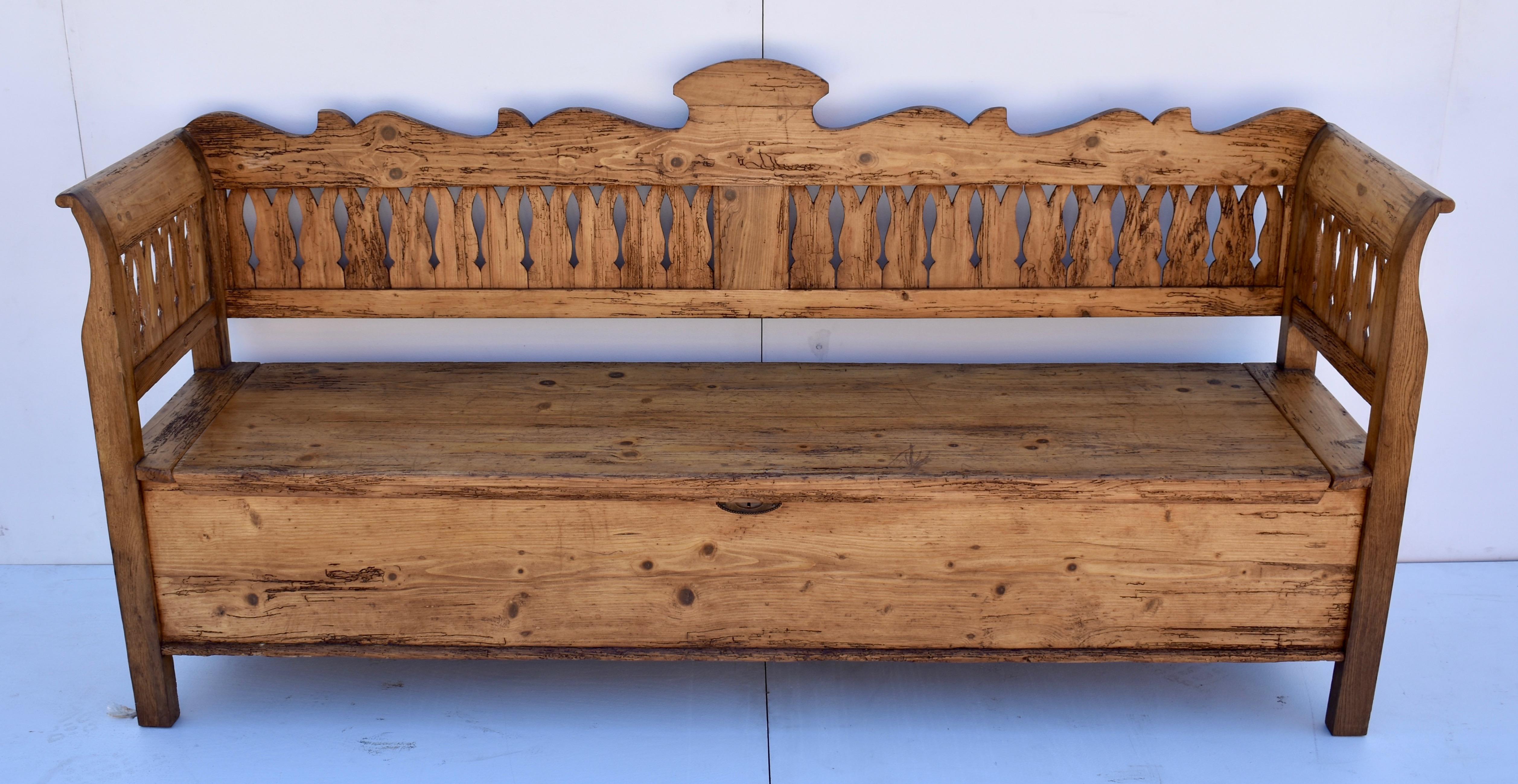 This stately pine and oak storage bench has a boldly scalloped back rail with a crest in the center. Pine splats run along the whole back, and the sides, where they are framed in the oak that comprises the integral arms and legs. The seat lifts to a