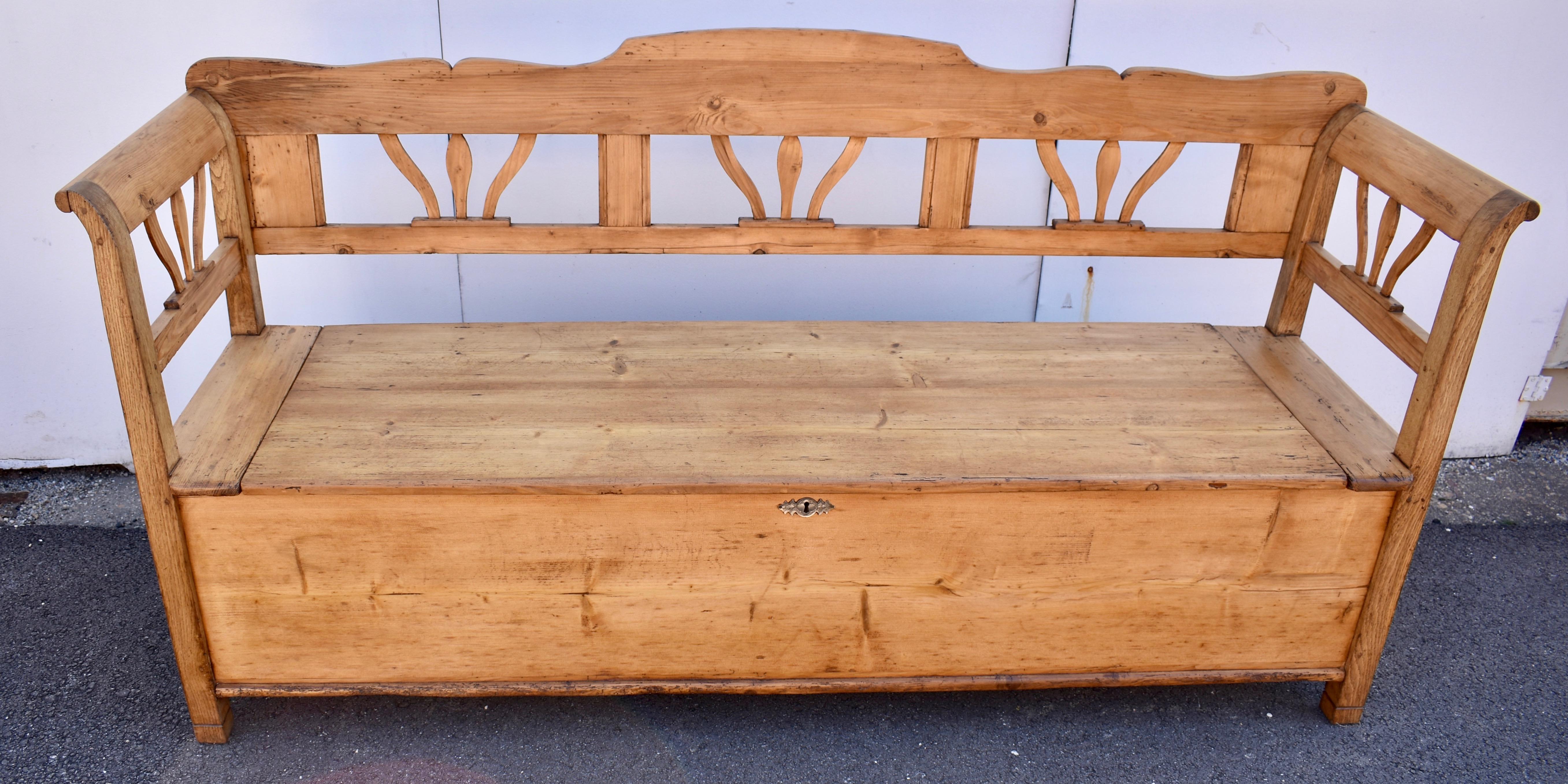 This excellent pine and oak storage bench features a scalloped top back rail which, with the bottom rail forms three “windows”, each framing three stylized floral splats.  The four legs are oak and with the pine side rails the same design is