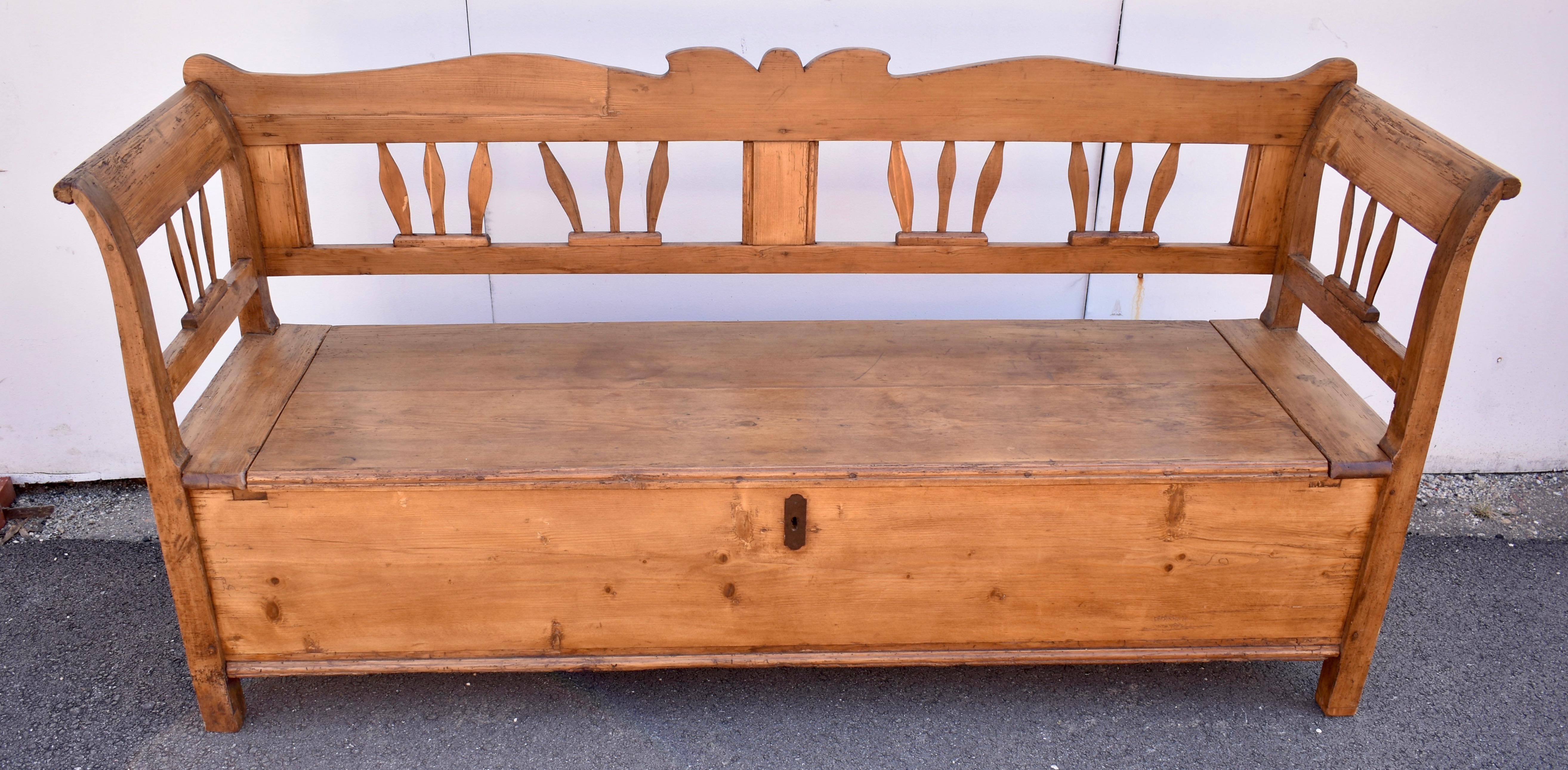 The back rail of this handsome pine and oak box bench crests in the center, then follows a broad and graceful line and ends in a little upturn in the back corners.  A central reeded splat divides the back space into two frames, each housing two