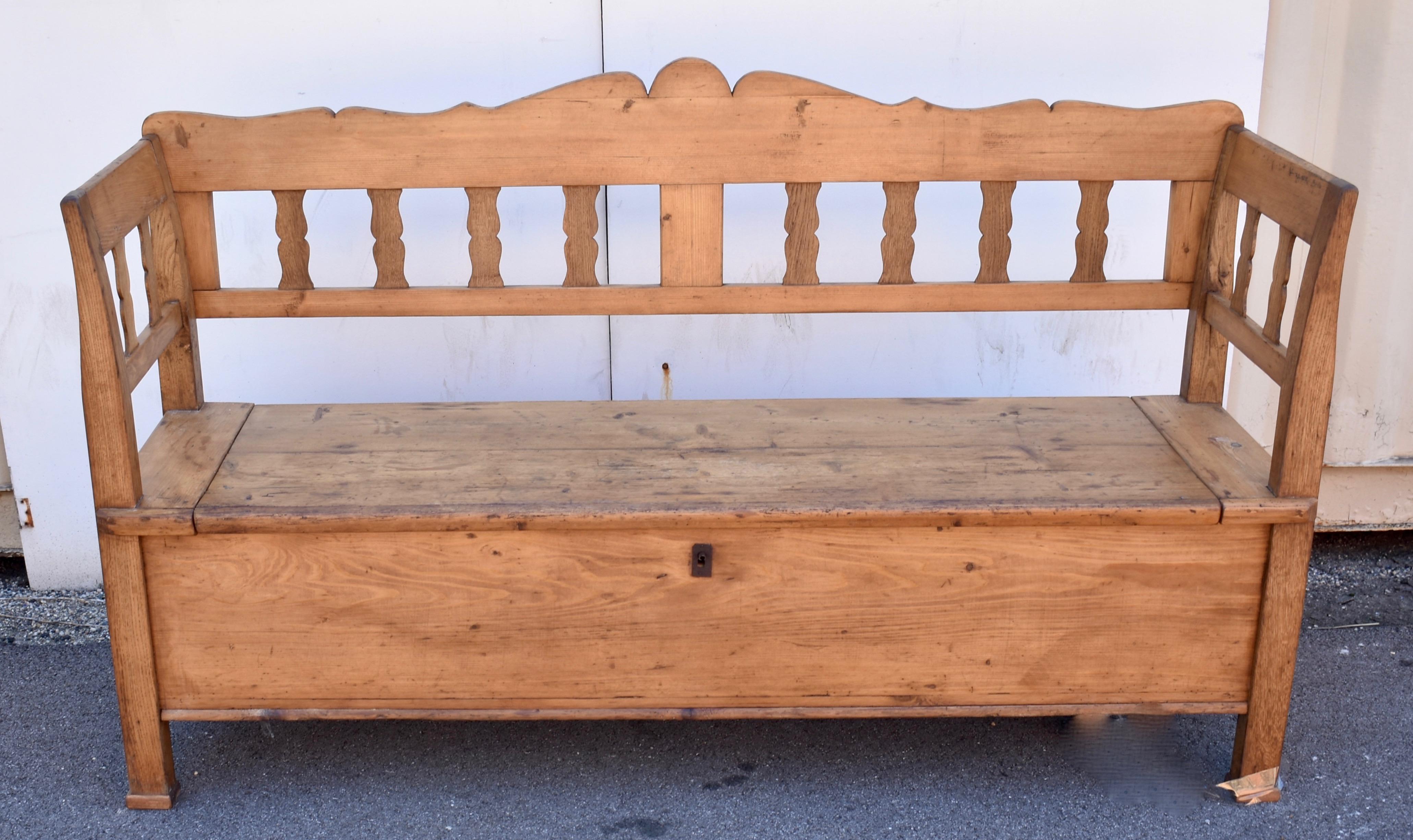 The scalloped top rail of this attractive box bench has its high point in the center and descends gently to meet the slightly scrolled oak stiles of the integral arms and legs.  A central splat creates two frames, each enclosing four flattened