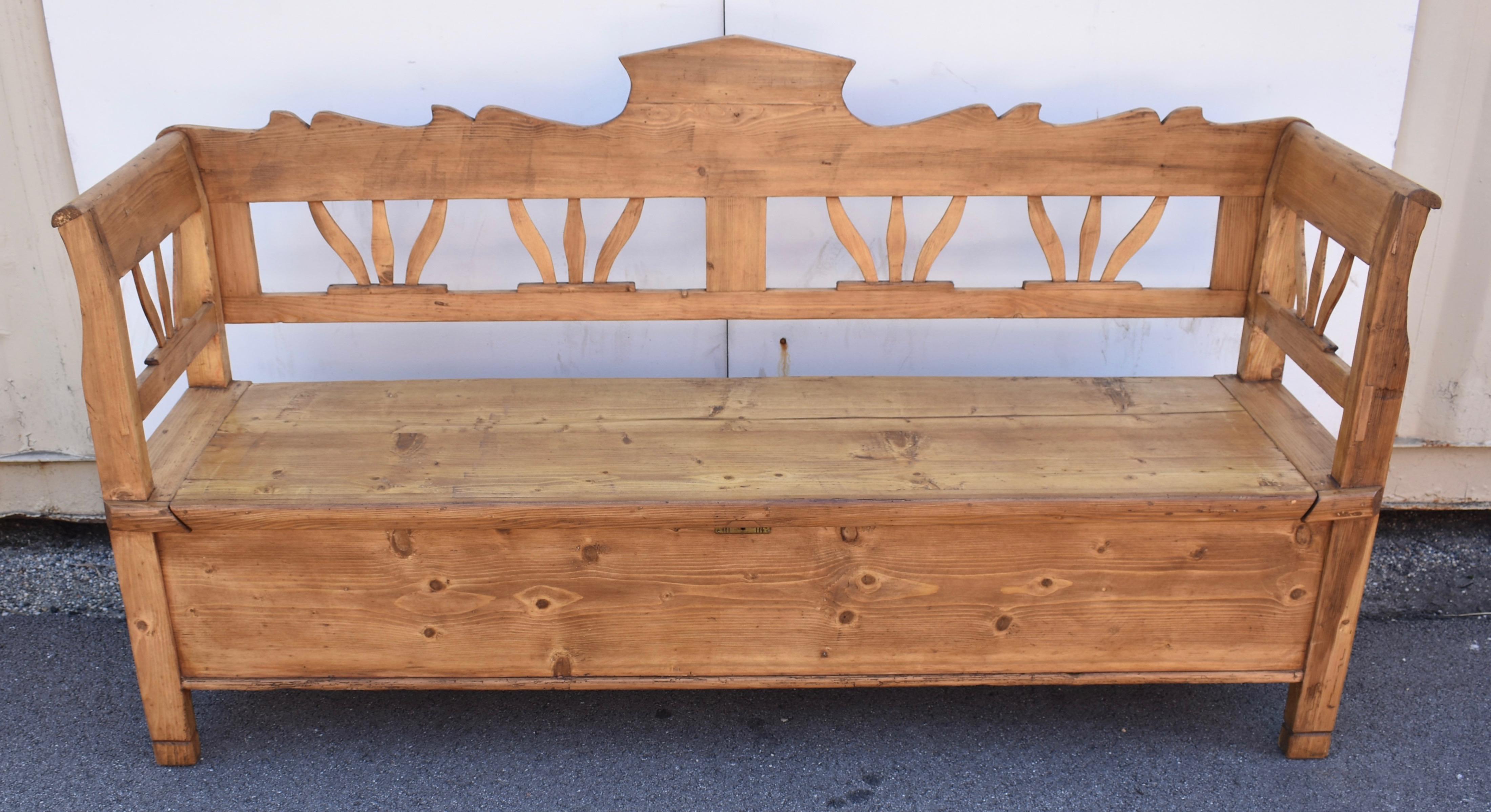 This large box bench has a boldly scalloped and crested top rail.  With the bottom rail and a central splat these form two frames each containing two stylized floral carvings.  These also feature in the arms.  The seat lifts on iron butt hinges to