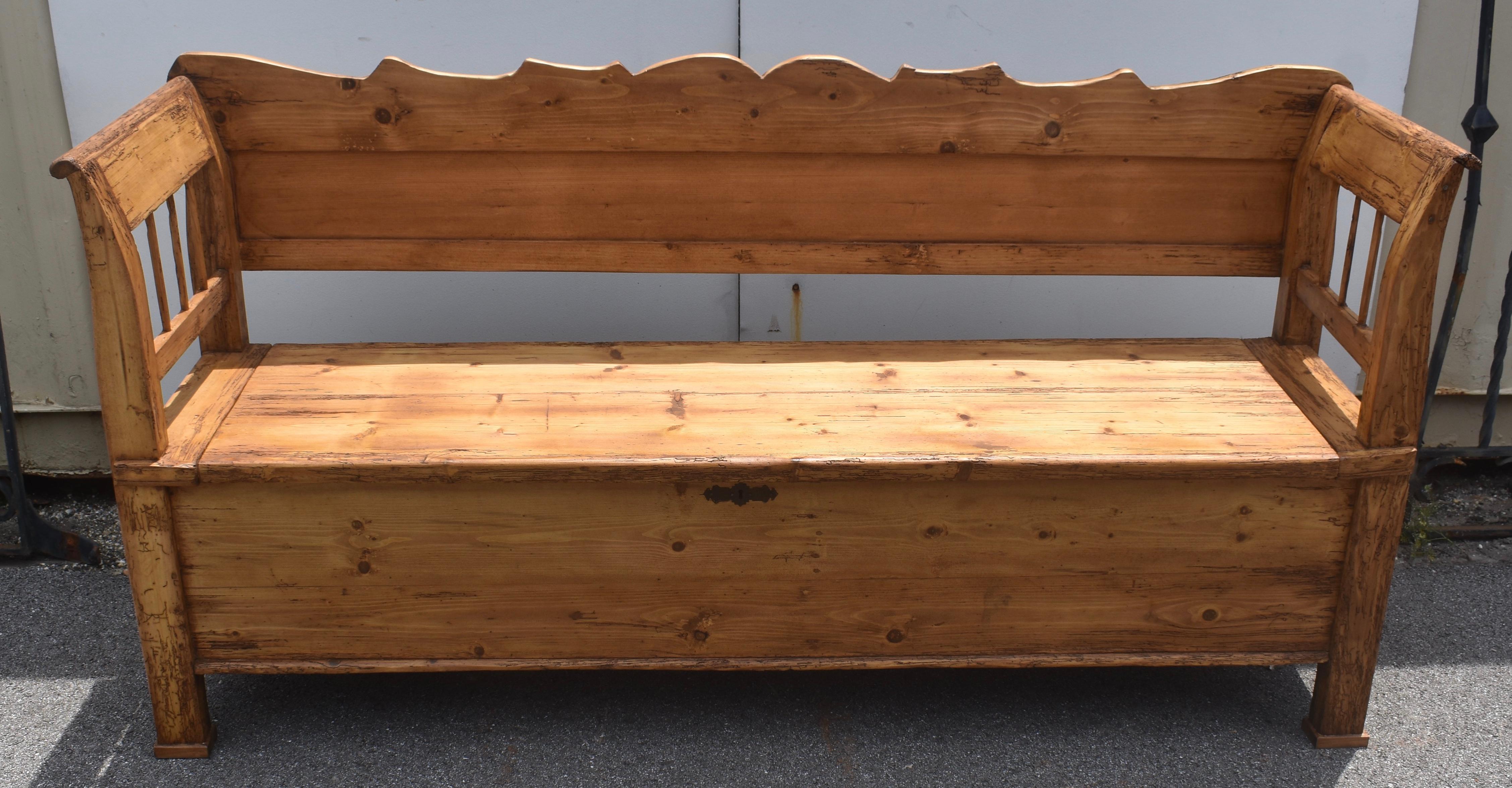 The scalloped top rail of this stately box bench might be better described as “rippled” or “wavy” as it sits above the long flat panel that, with the bottom rail, constitutes the back.  The integral arms and legs stand straight, then scroll gently