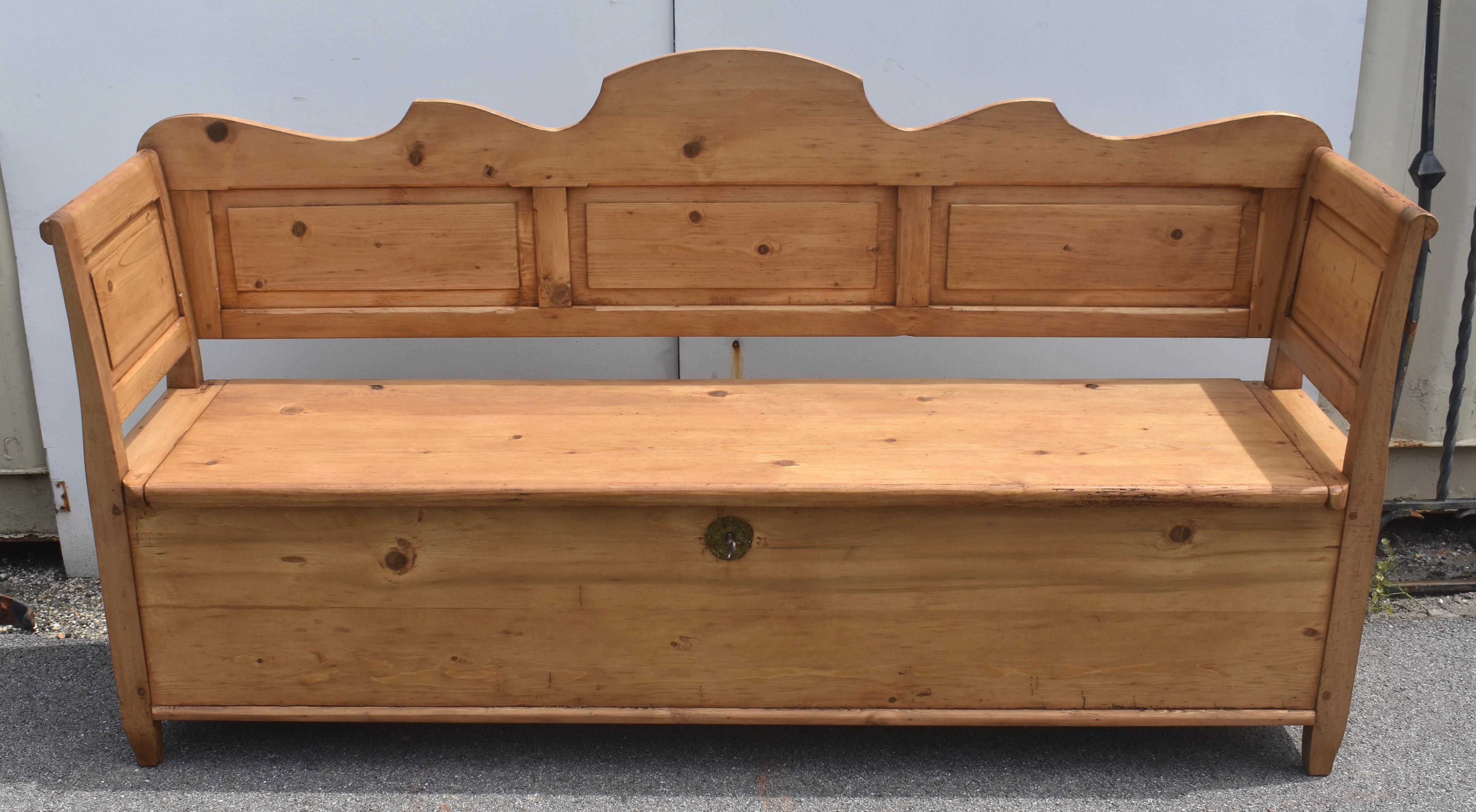 La traverse supérieure de cet imposant Box Bench est audacieusement festonnée et s'élève jusqu'à une crête arrondie au centre ; la traverse inférieure est droite.  Quatre larges montants encadrent trois panneaux rectangulaires simples en relief. 