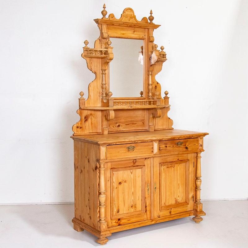 Decorative elements abound in this striking pine buffet server from the late 1800's. Turned columns, finials, and a mirror all add to the strong visual impact. The upper section has stylized shelving to show off items on display while the lower