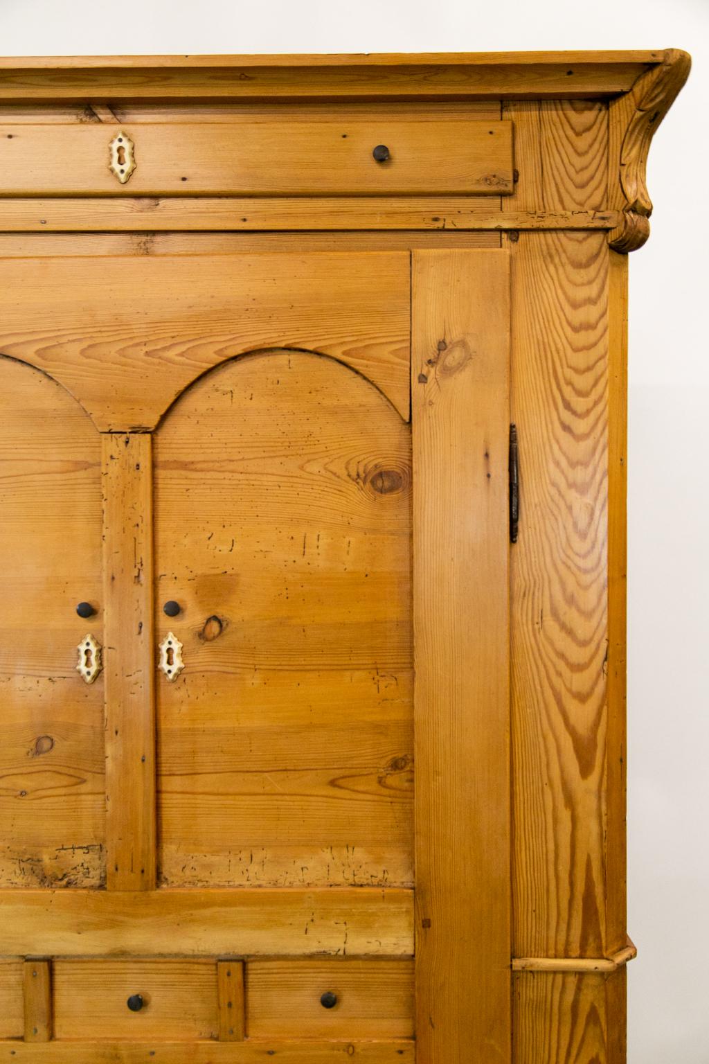 This unusual pine armoire has an entirely dummy front including the door, upper frieze drawer, and lower base drawer. The interior has sixteen coat hooks and one adjustable shelf. There is one fixed shelf in the lower area. The door has raised