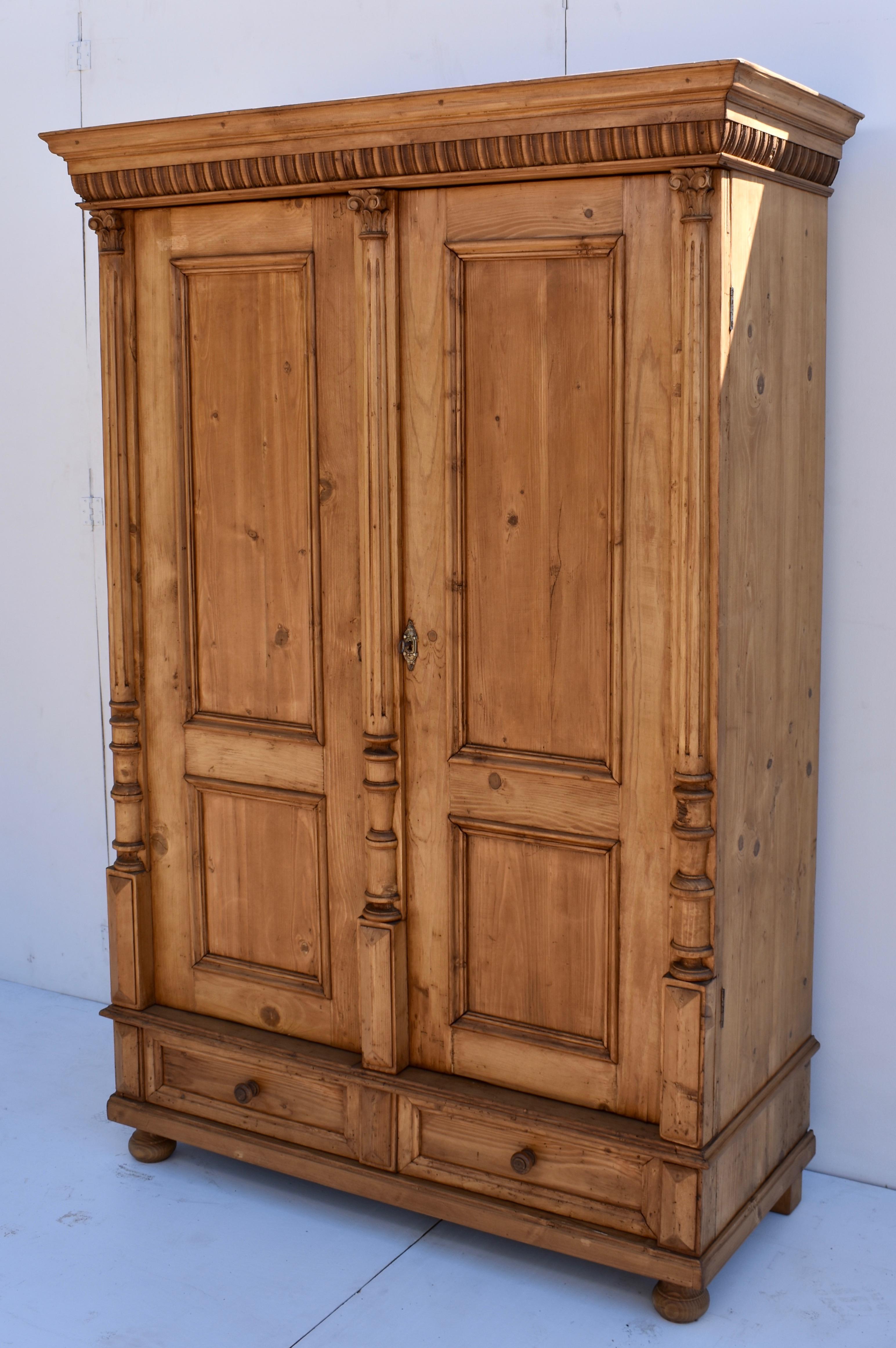 This is a very attractive example of a central European two door wardrobe. The crown molding is bold and decorative and sits above two doors, each with two panels. The doors are flanked and separated with applied fluted split columns on rectangular
