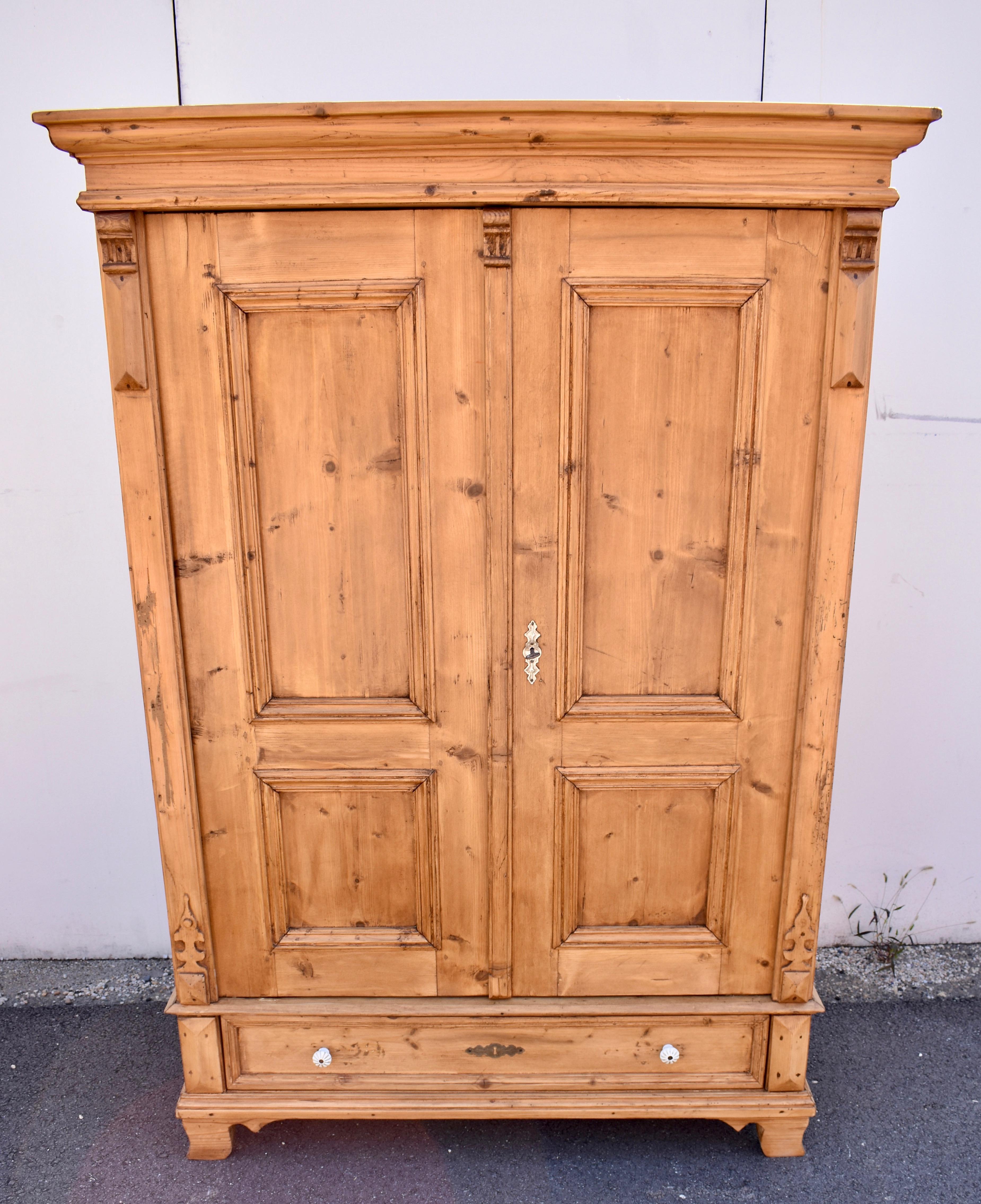 The bold ogee crown molding incorporates a horizontal reeded strip and sits on a plain frieze on this sturdy armoire.  The door frames are thick, and enclose two flat panels on each door.  The front corners  are dressed with carved hardwood corbels