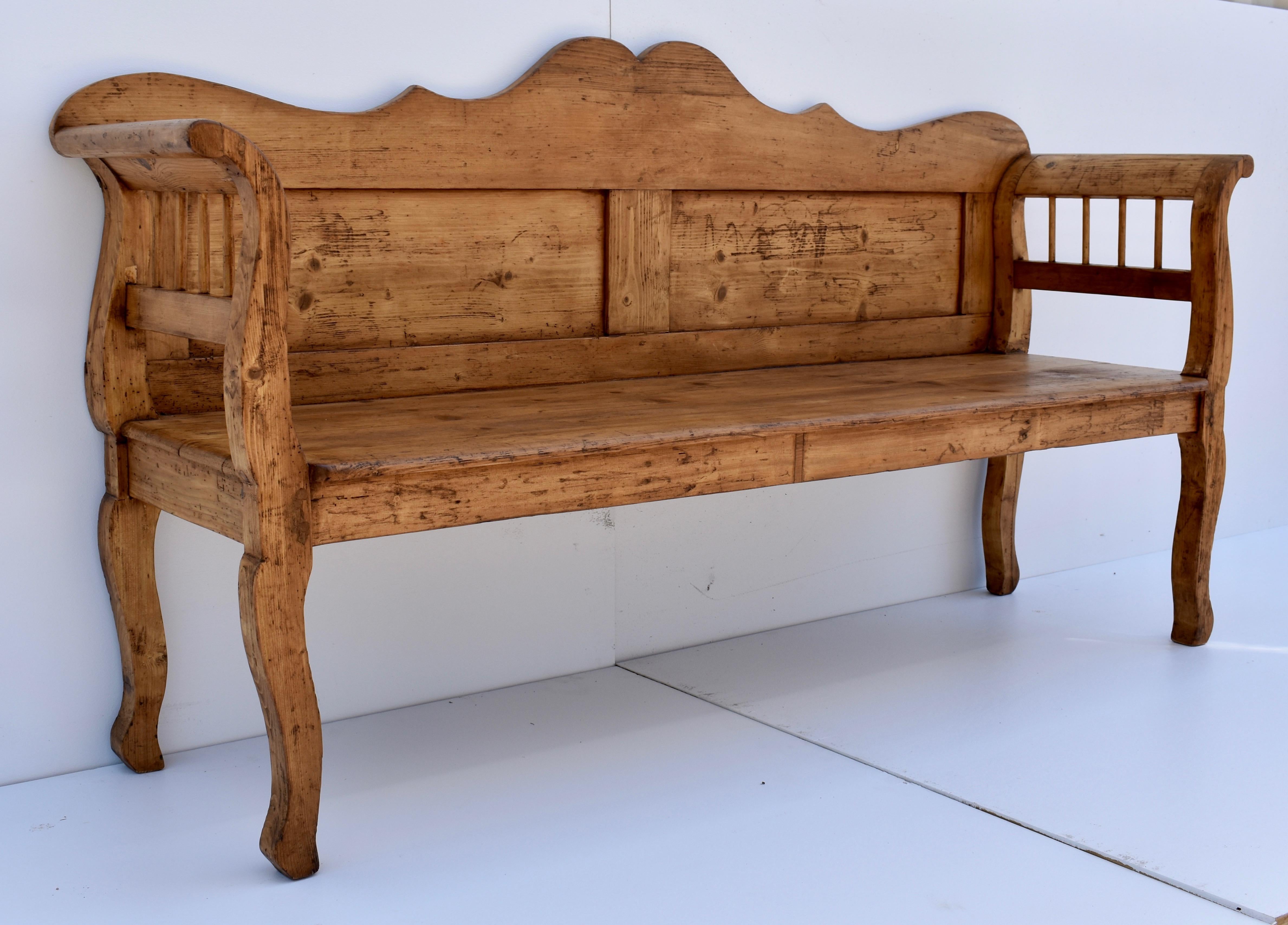 This shapely pine bench or settle has a scalloped top rail to the back, above two enclosed flat panels. The integral arms and legs have a beautiful curvilinear form and incorporate a row of turned spindles. The deep seat is firm and comfortable.