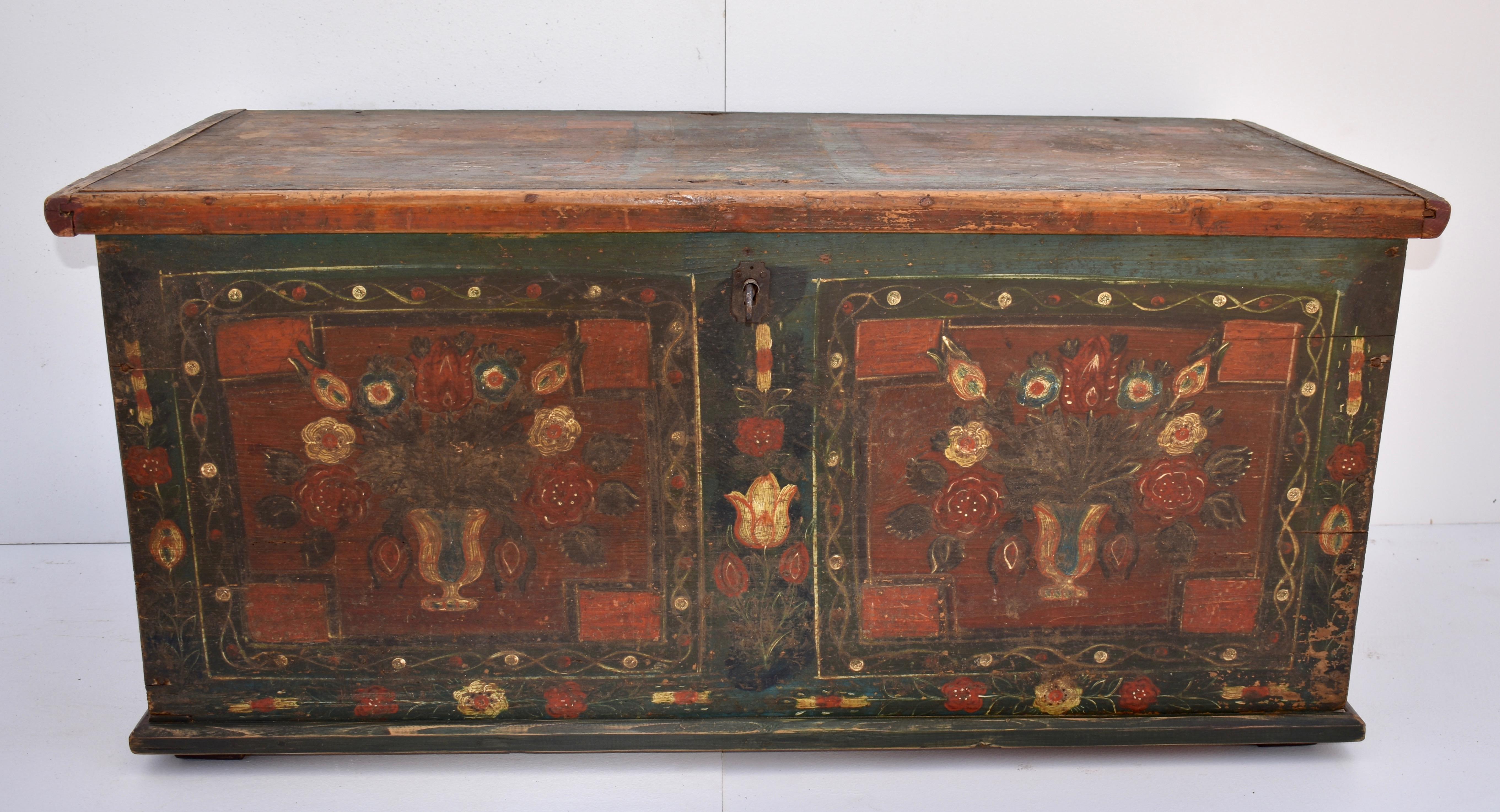 This beautifully painted primitive trunk is nailed rather than dovetailed. The front bears two stylized urns of flowers within painted panels with multicolored floral work between and around them. The sides show a bouquet of flowers, tied with a