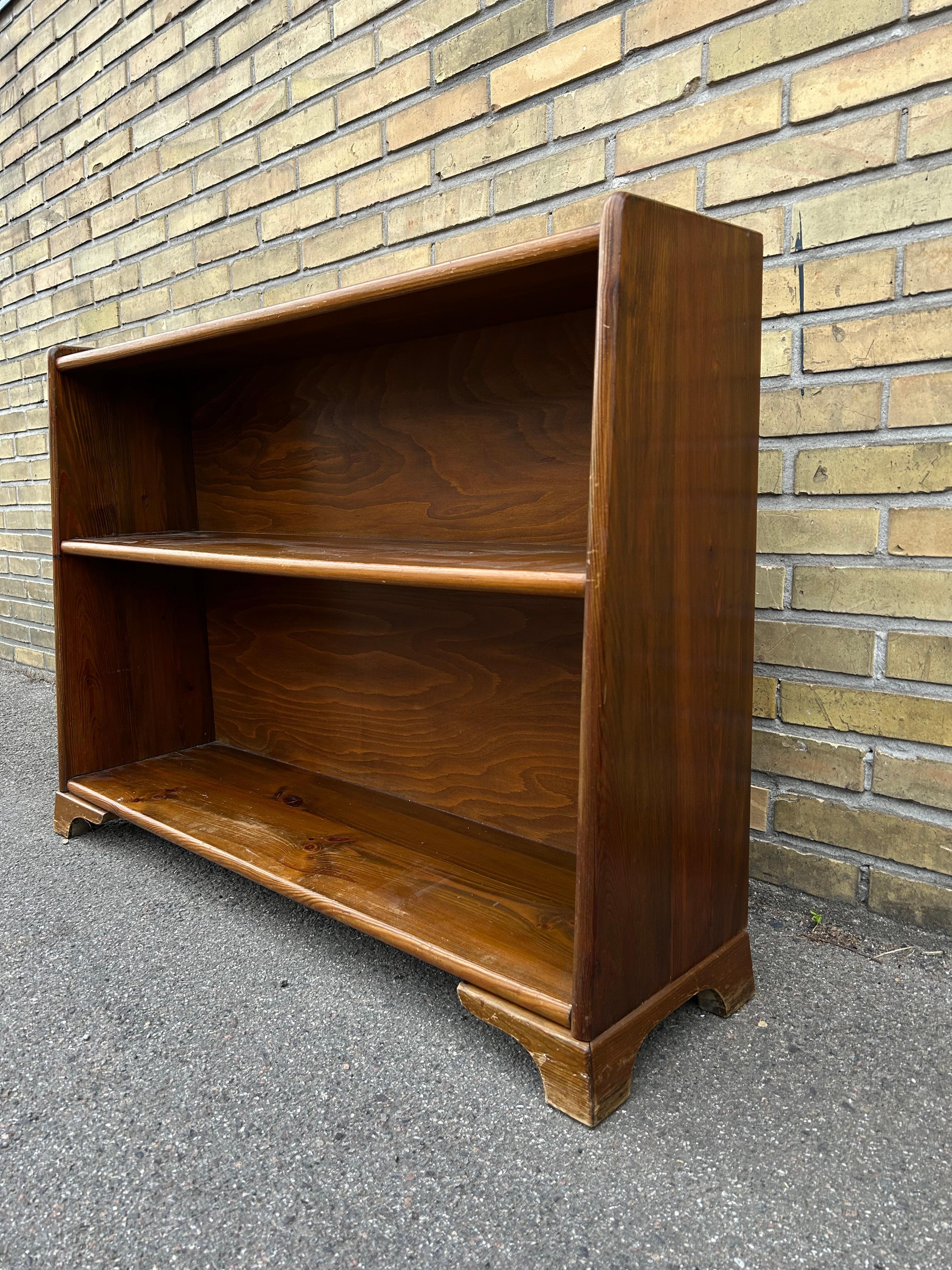 Rare patinaed book shelf by an unknown Swedish cabinetmaker in solid acid stained pine wood.
The shelf consists of two shelf’s and very art deco inspired feet and raised edges on the top of the shelf.

The book shelf if similar to pieces by