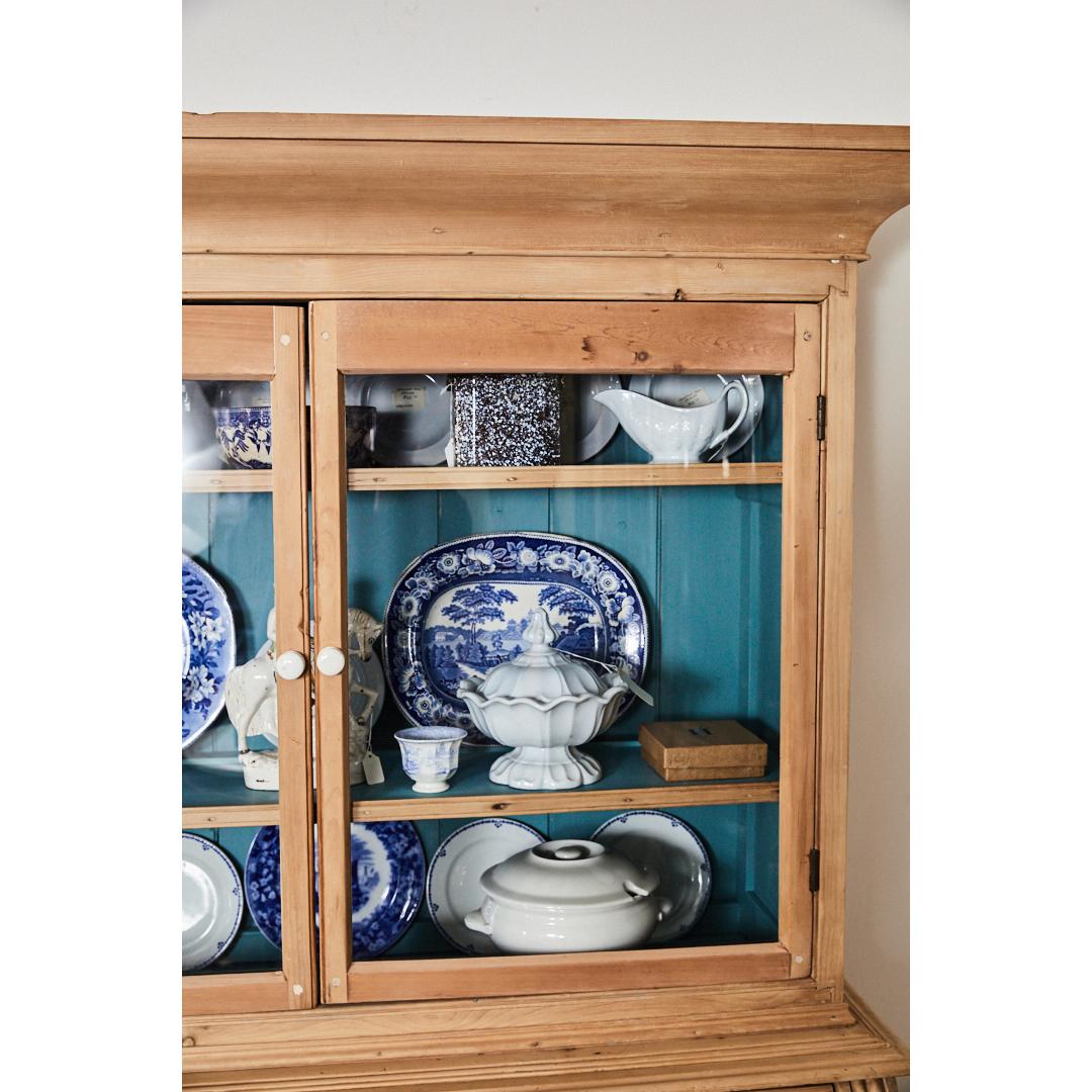 A handsome piece of English pine furniture, this cabinet has two doors with a blue painted interior and two shelves over two small and two larger drawers. The piece has white ceramic knobs. The piece stands on four shaped feet. Solidly constructed,