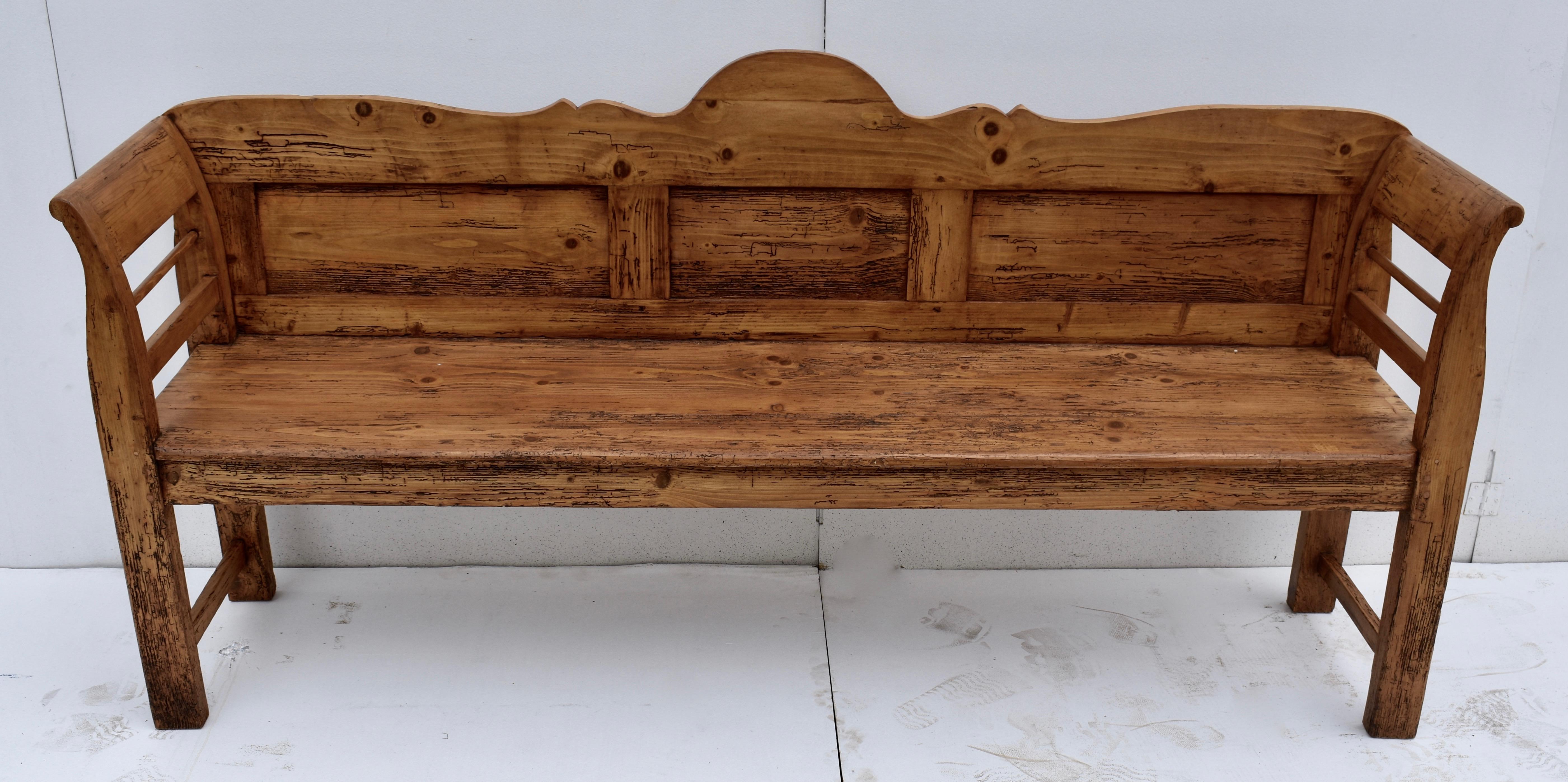 This long, low bench or settle is the epitome of rustic charm. The arched and scalloped top rail sits above three flat panels while the scrolled arms frame a horizontal spindle and stretcher, this latter repeated low in the leg. The deep seat is